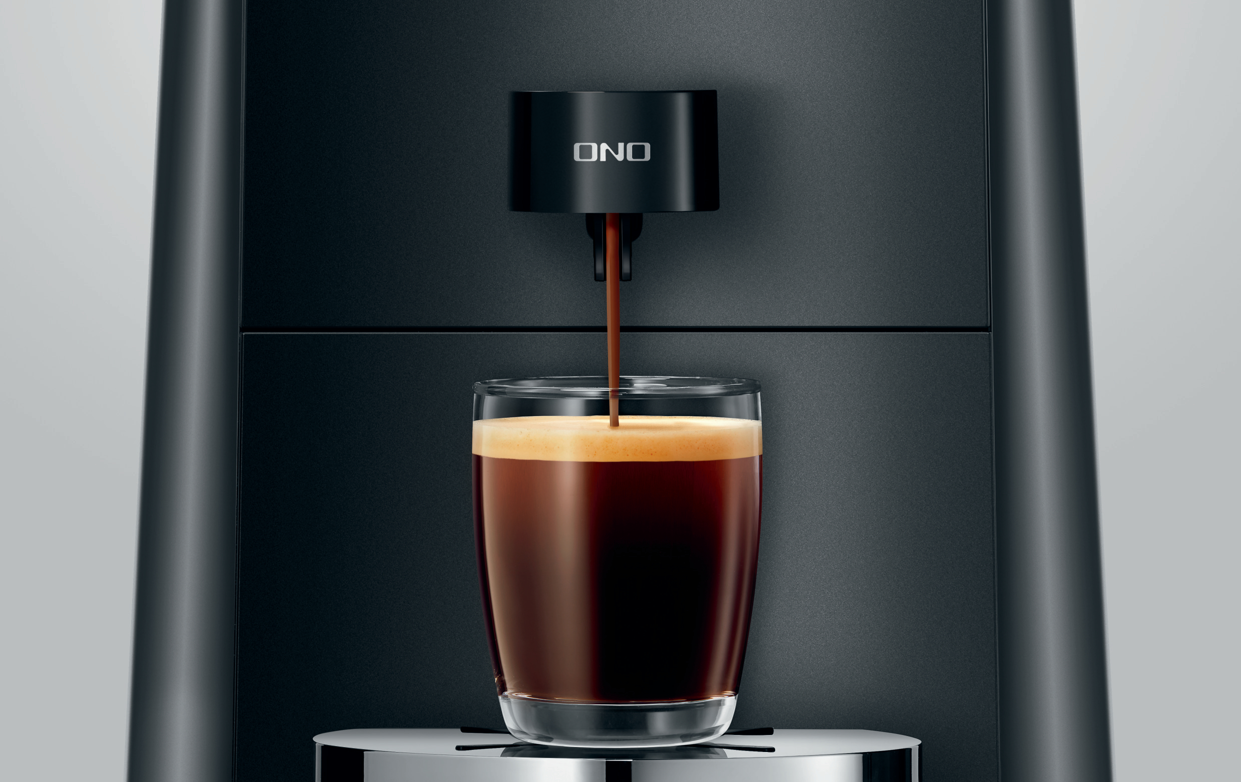 Eine Kaffeemaschine, die Kaffee in ein Glas ausgibt. Die Maschine ist schwarz, der Kaffee dunkel, das Glas klar.