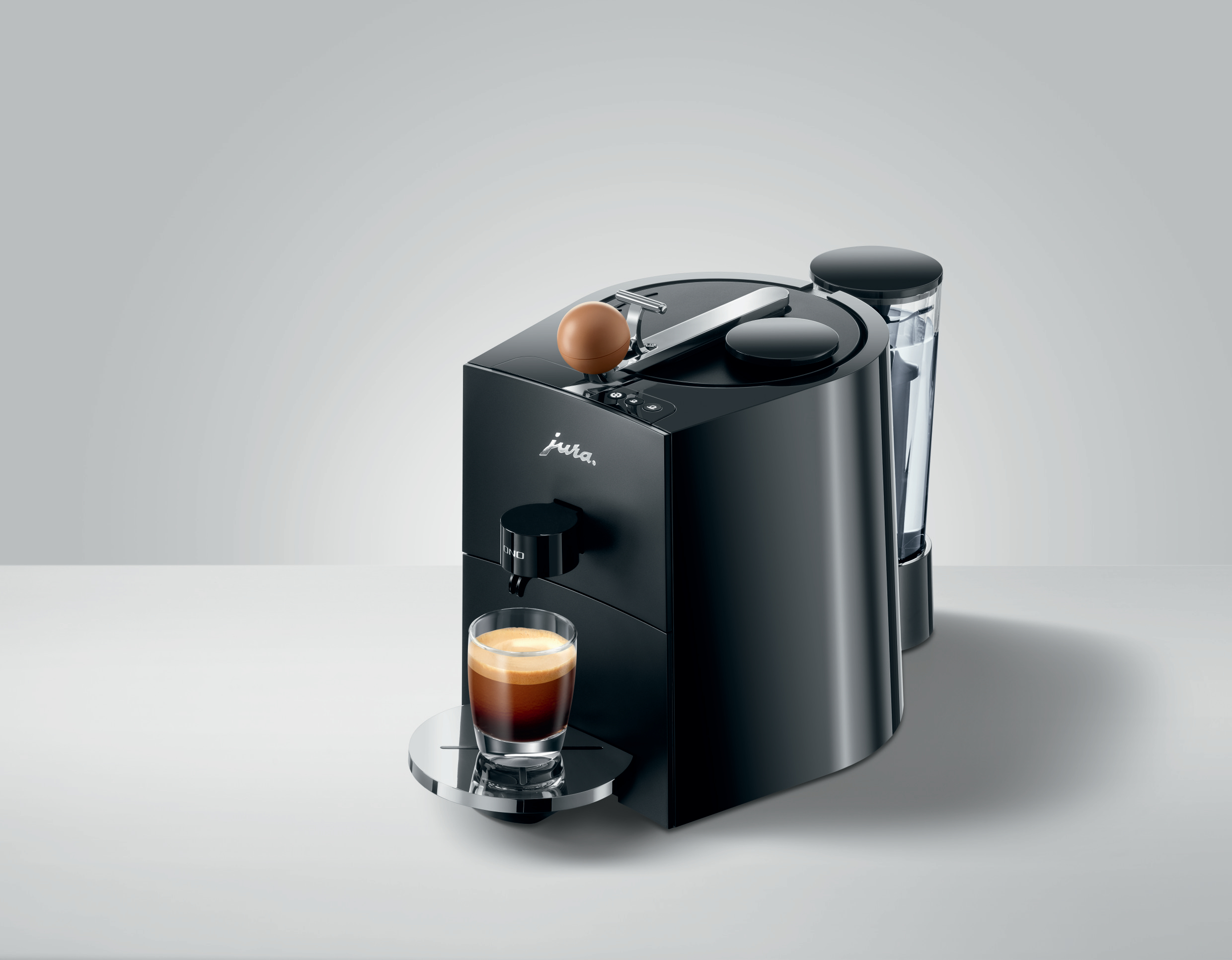 Schwarze Jura Kaffeemaschine mit einem Glas Espresso und einem Wasserbehälter auf weißer Oberfläche.