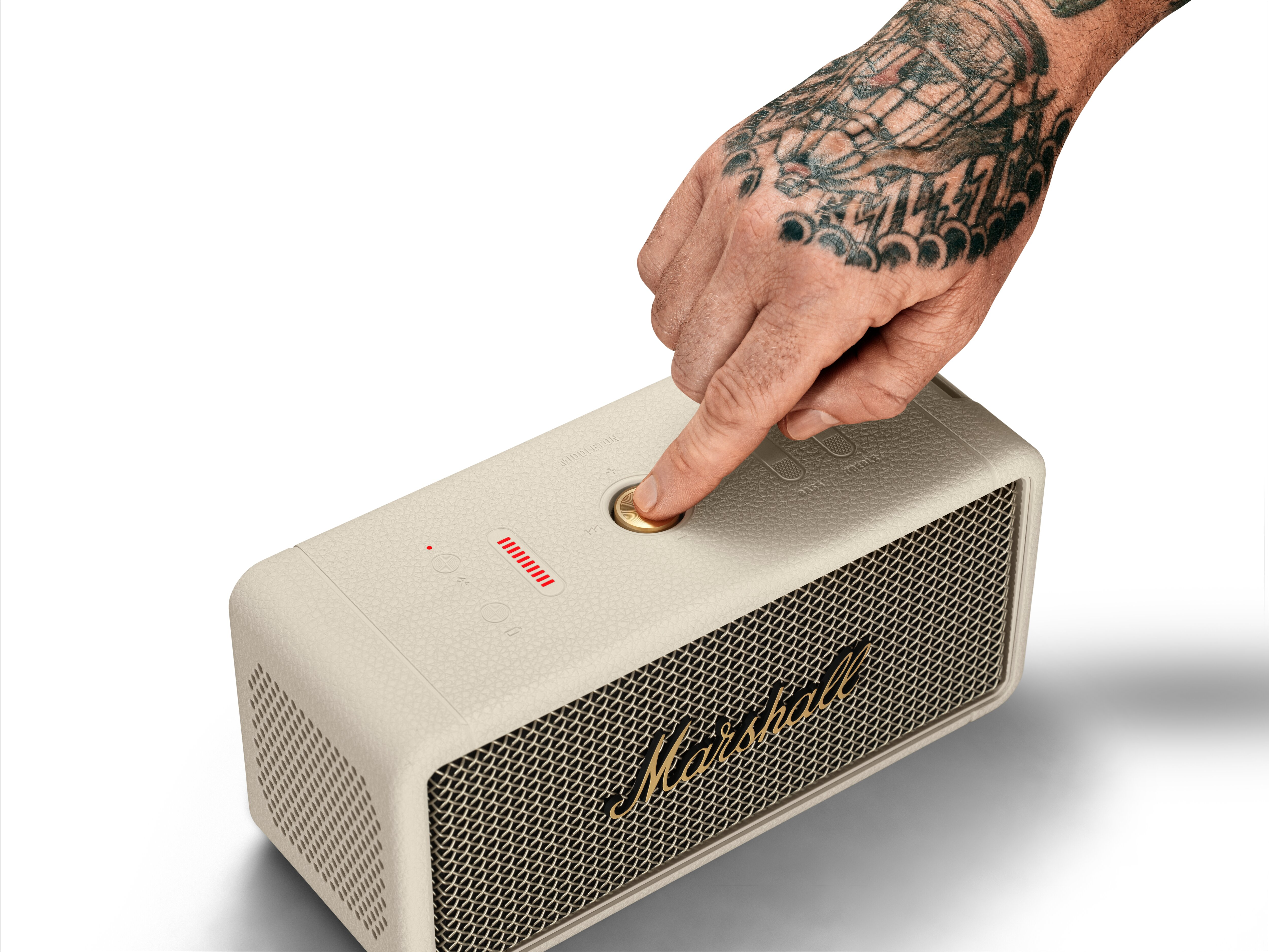 Eine Hand mit Tattoo drückt einen goldenen Knopf auf einem Lautsprecher. Der Lautsprecher ist beige.