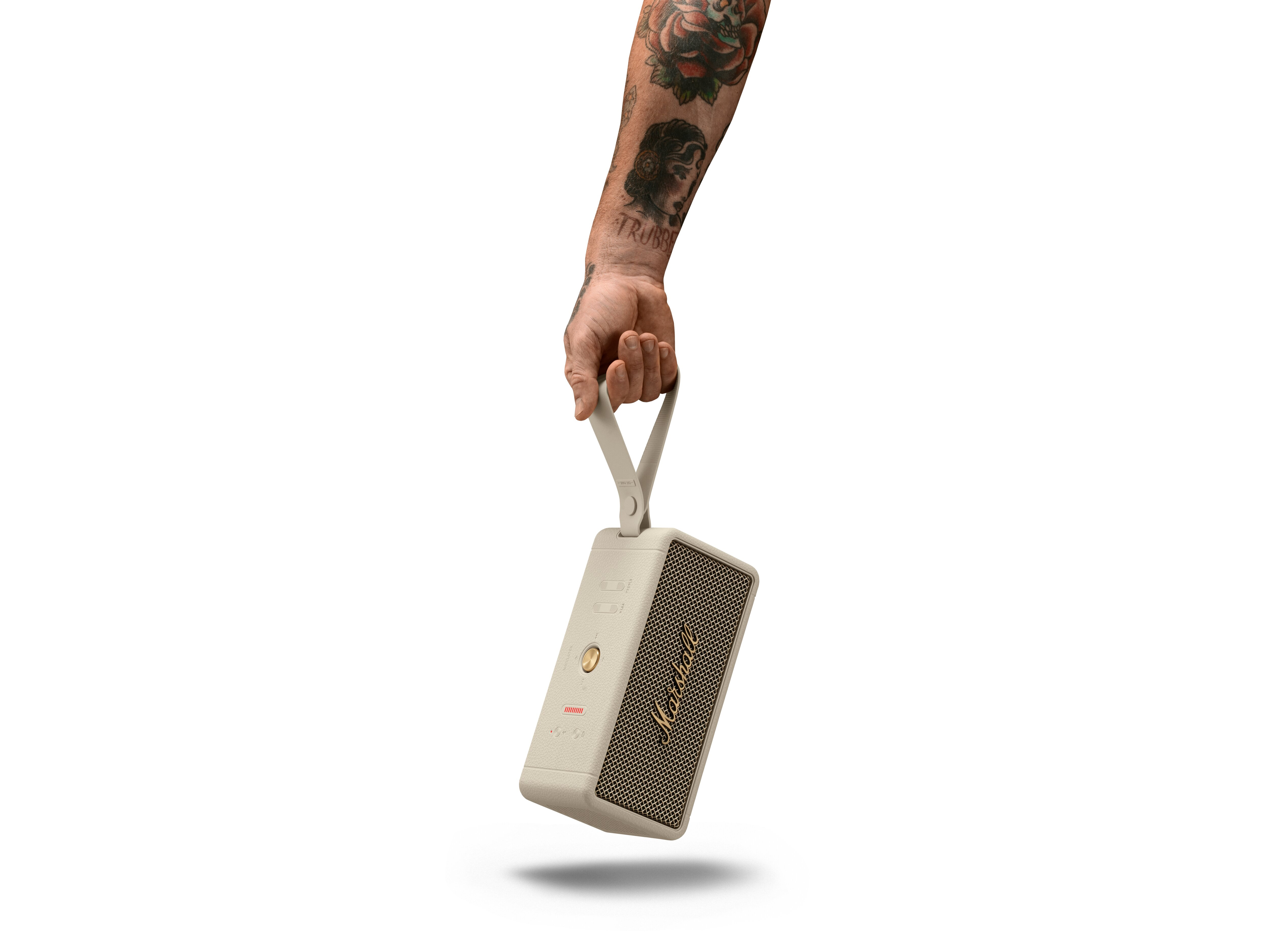 Ein tätowierter Arm hält einen beigen und goldenen Marshall-Lautsprecher vor weißem Hintergrund.