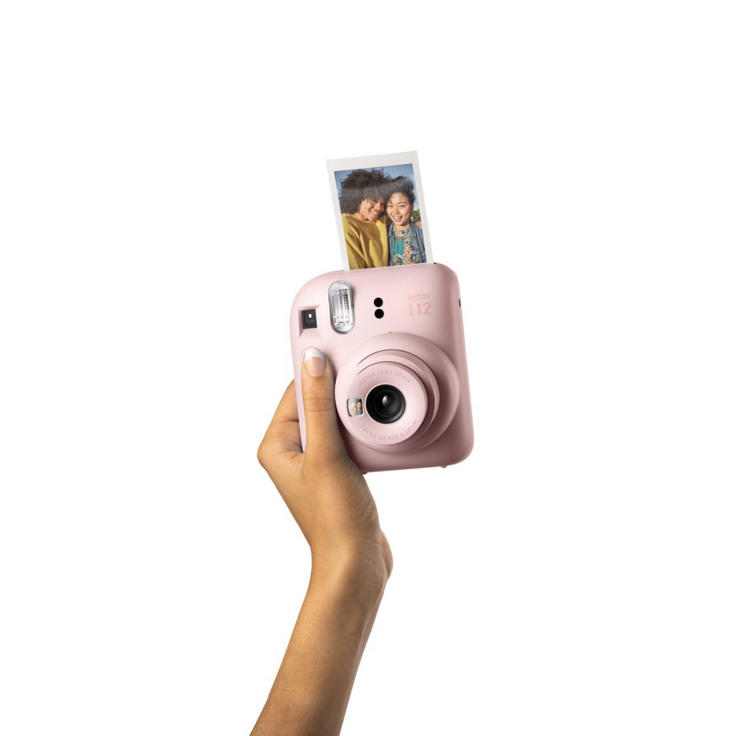 Roze Instax camera in een hand. Een foto wordt uitgeworpen. Witte achtergrond.