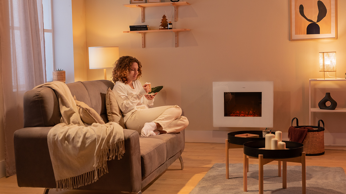 Mujer en un sofá con un bocadillo. Chimenea, lámparas y mesas en un salón acogedor.