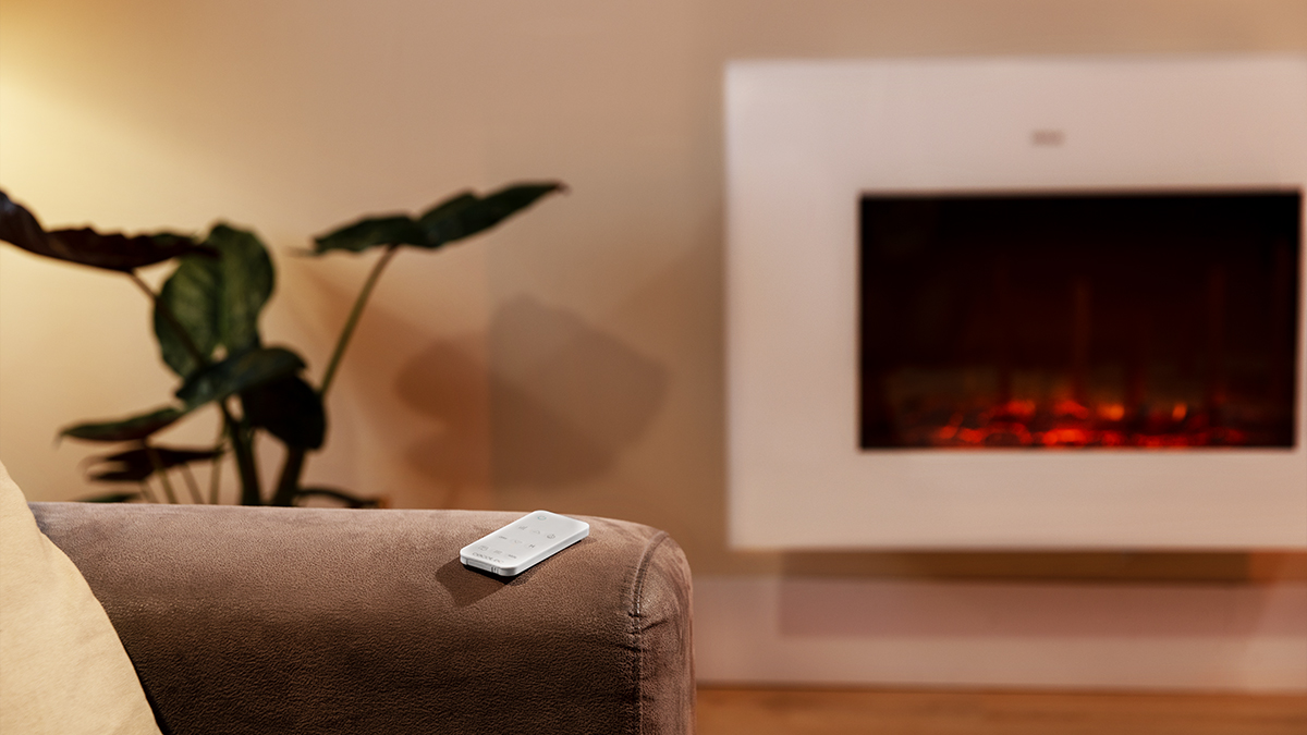 Escena de sala. Un mando a distancia en un sofá marrón, una planta y una chimenea con llama brillante son visibles.