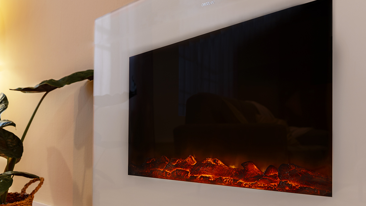 Chimenea eléctrica en una pared. Tiene una pantalla negra con llamas naranjas en la parte inferior. Una planta está a la izquierda.