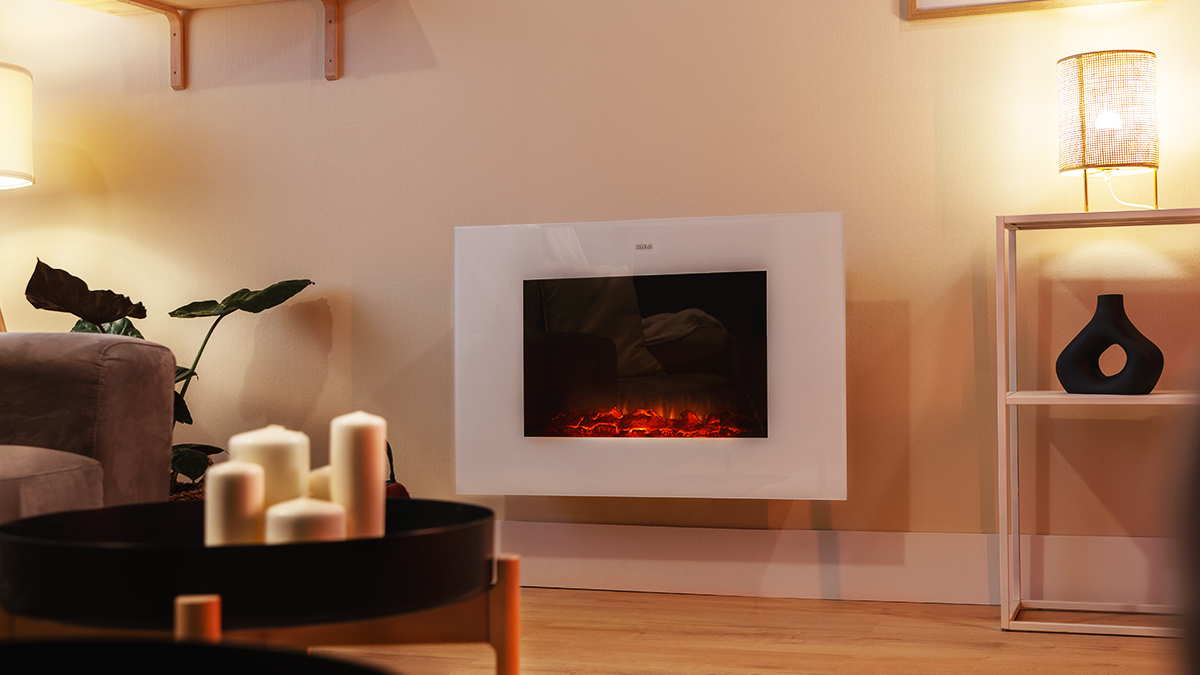 Salón con chimenea eléctrica, velas, jarrón negro en estante y sofá. Ambiente cálido y acogedor.