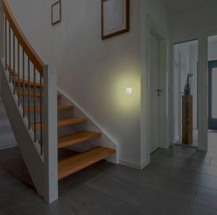 Treppe mit Holzstufen, weißen Wänden und einer Leuchte. Im Hintergrund Türen und Flur.