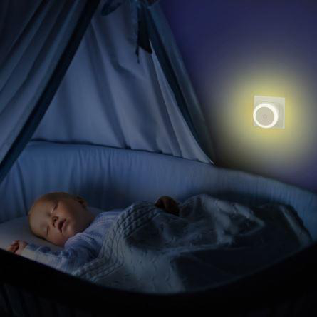 Ein Baby schläft in einem Kinderbett mit einem Nachtlicht an der Wand.