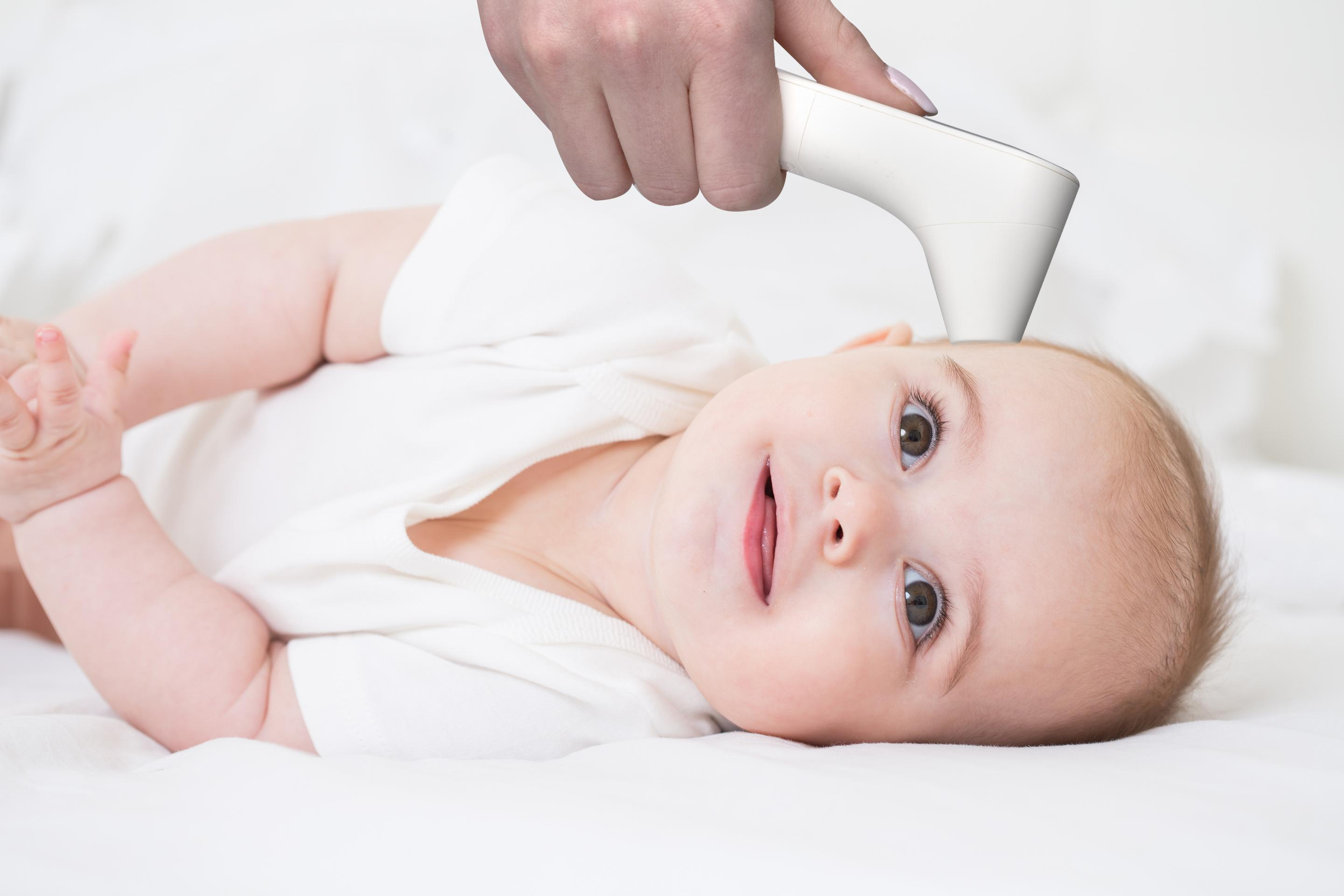 Ein Baby liegt auf einer weißen Decke, ein Thermometer wird benutzt.