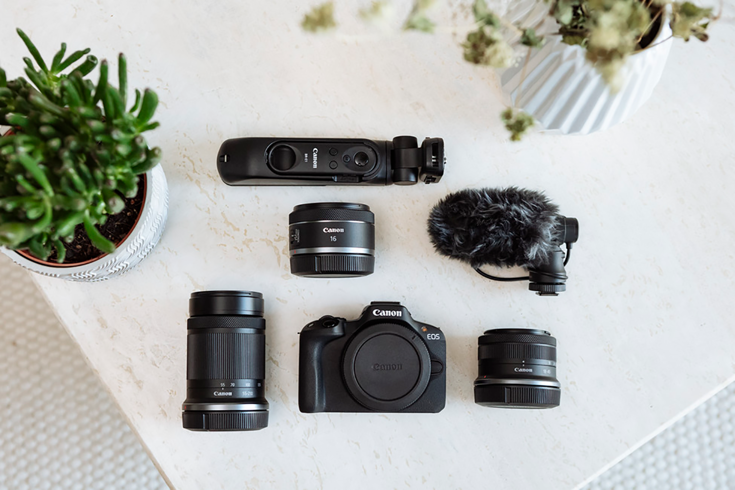 Overhead shot of Canon camera equipment on a white table. Lenses, microphone, and camera.