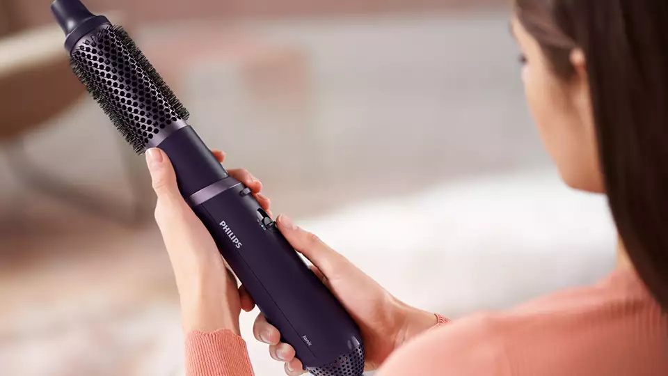 Frau hält einen Philips Haarstyler. Er ist dunkelviolett mit Bürstenkopf und Knöpfen.