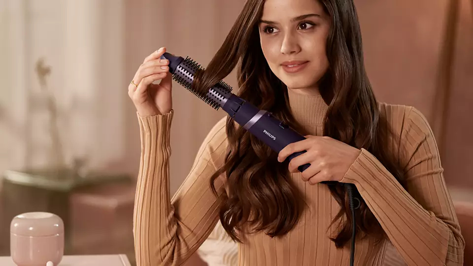 Eine Frau, die einen Philips Haarstyler auf ihrem langen braunen Haar verwendet.
