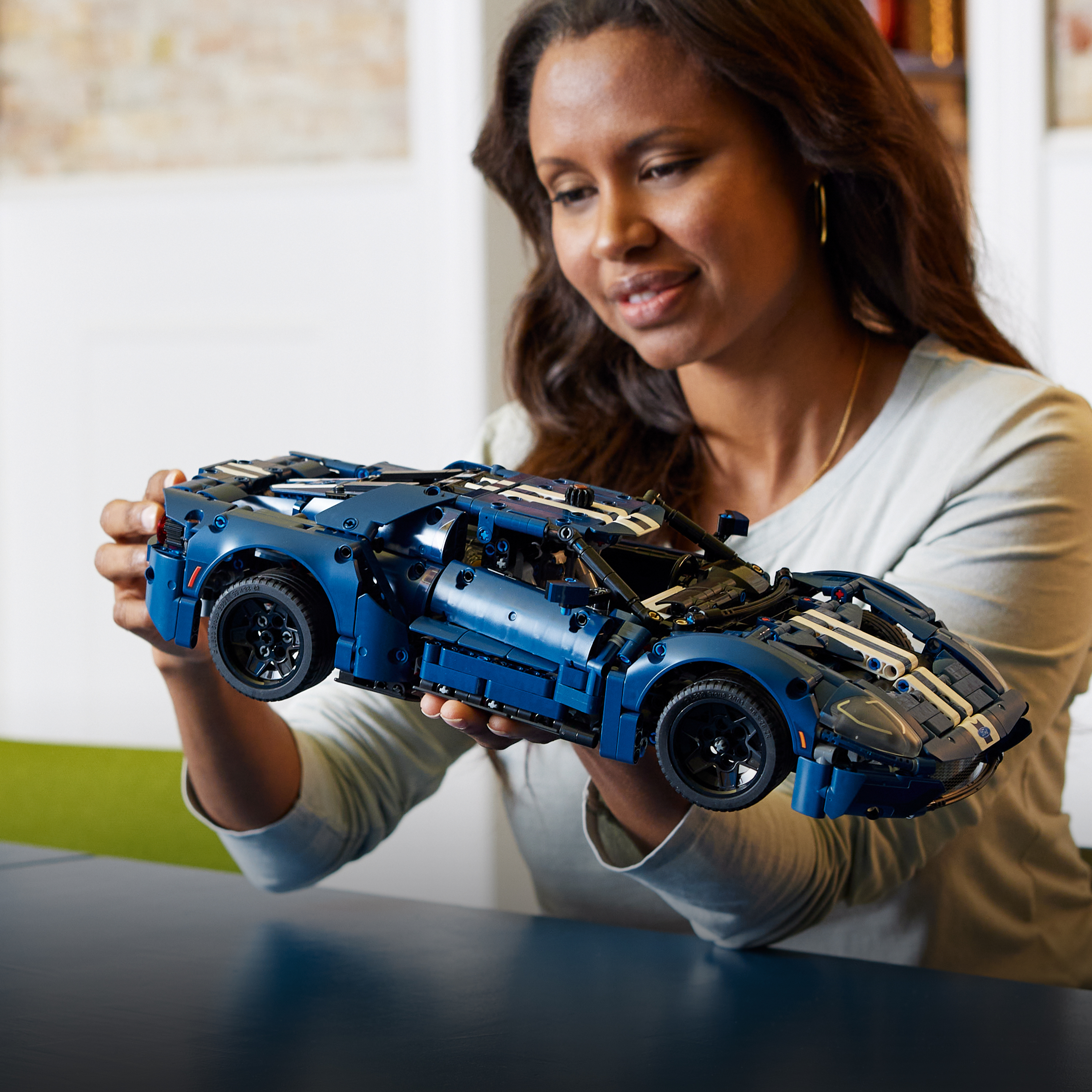 Frau hält ein blaues Lego Ford GT-Auto. Das Auto steht im Fokus, Details sind sichtbar.
