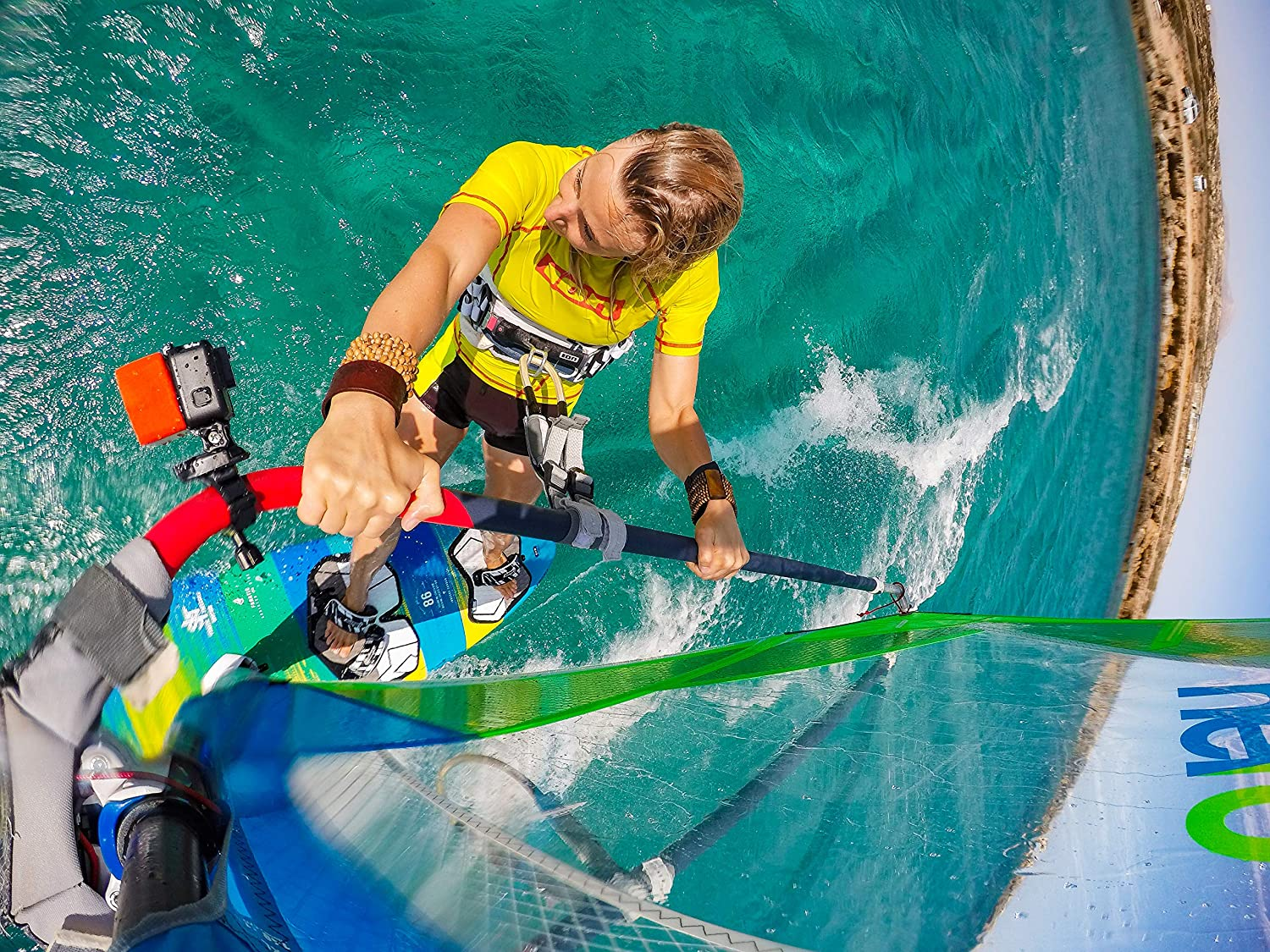 Una persona practicando windsurf en agua turquesa, sosteniendo una vela.