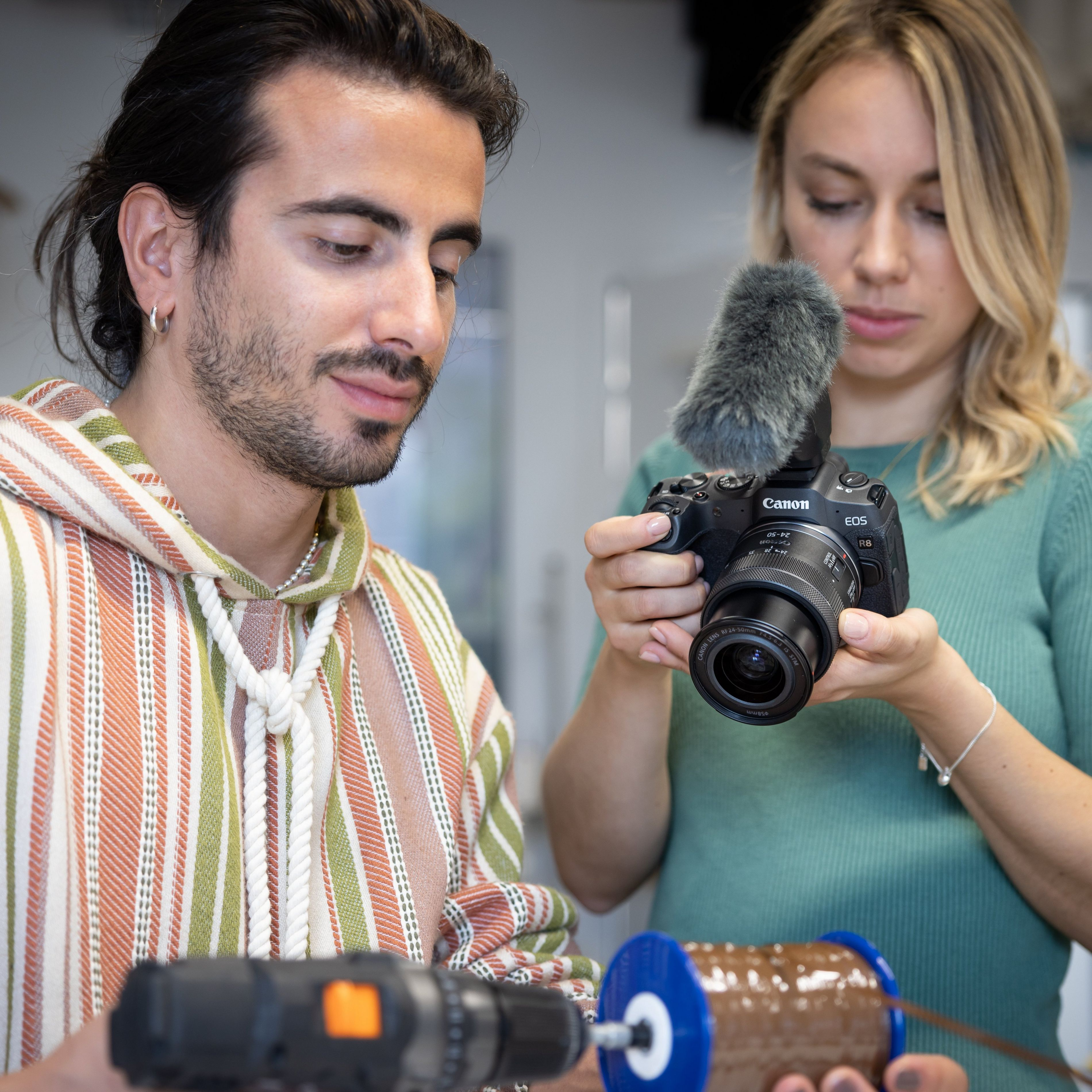 Uomo con felpa a righe e donna con macchina fotografica, bobina marrone in primo piano.