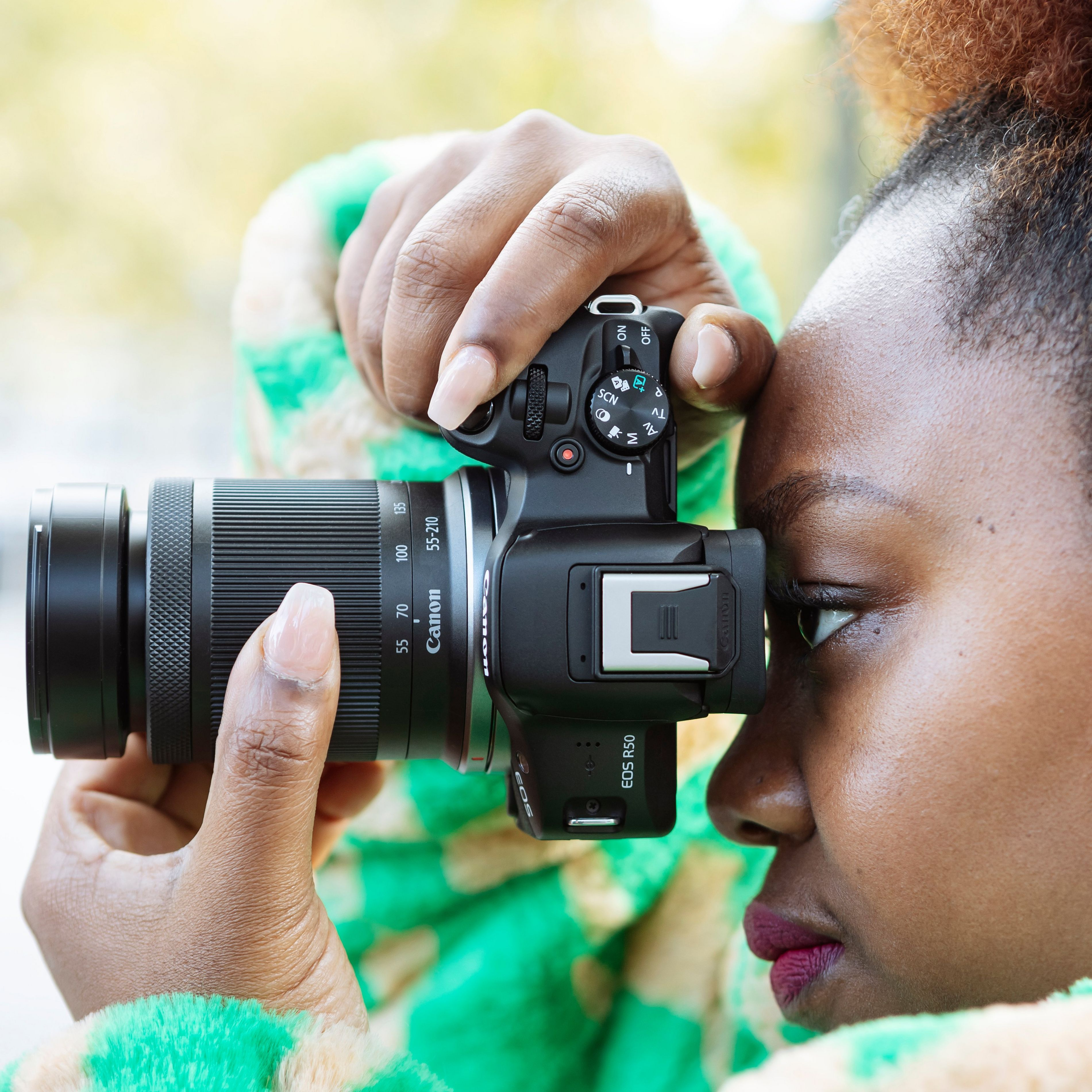 Une femme tenant un appareil photo Canon contre son œil, en train de prendre une photo.