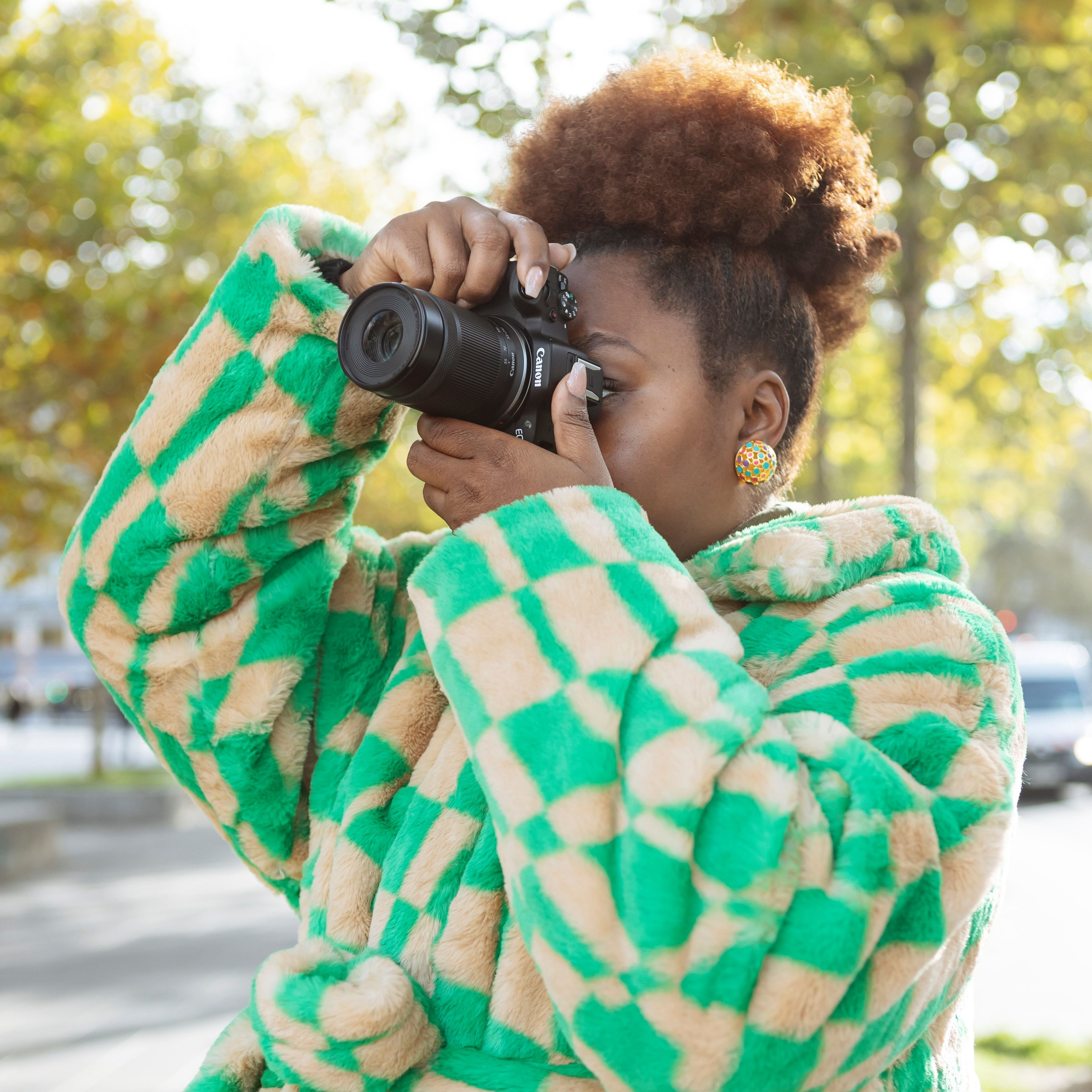 Une personne prend une photo avec un appareil photo, portant un manteau à carreaux vert et beige.
