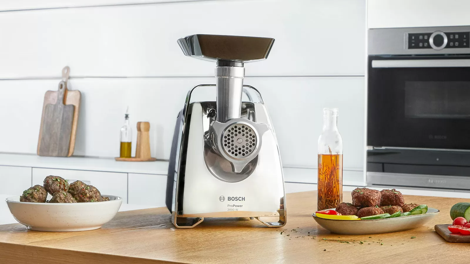 Rozsdamentes acél húsdaráló egy tál húsgombóccal és olajjal.