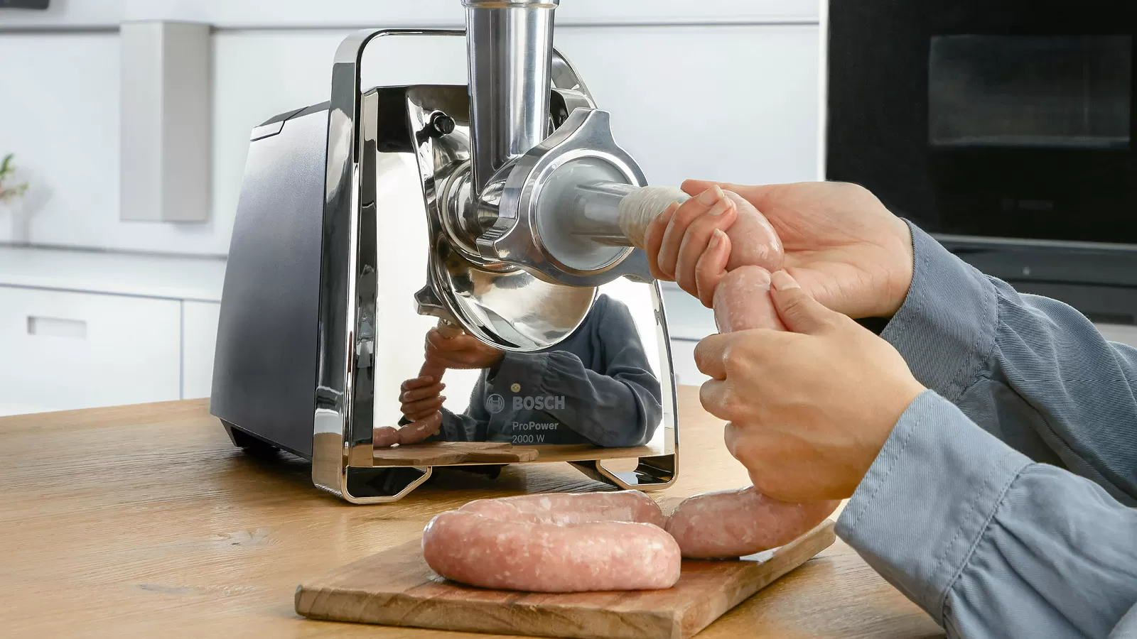 Személy kolbászt tölt be a tokba húsdarálóval. Fa felület a háttérben.