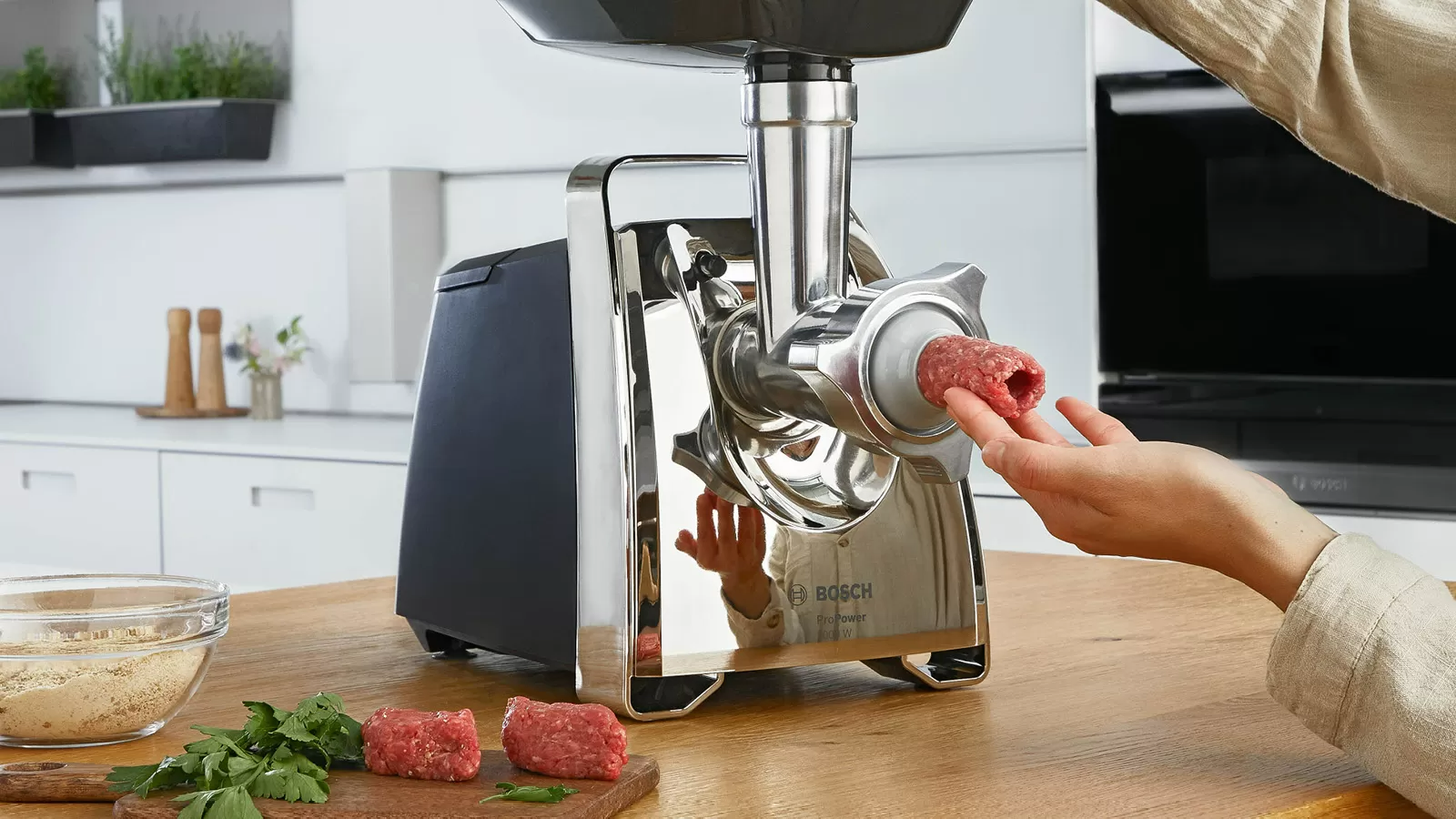 Egy személy húsdarálót használ. Nyers hús, egy tál és egy vágódeszka van a közelben.