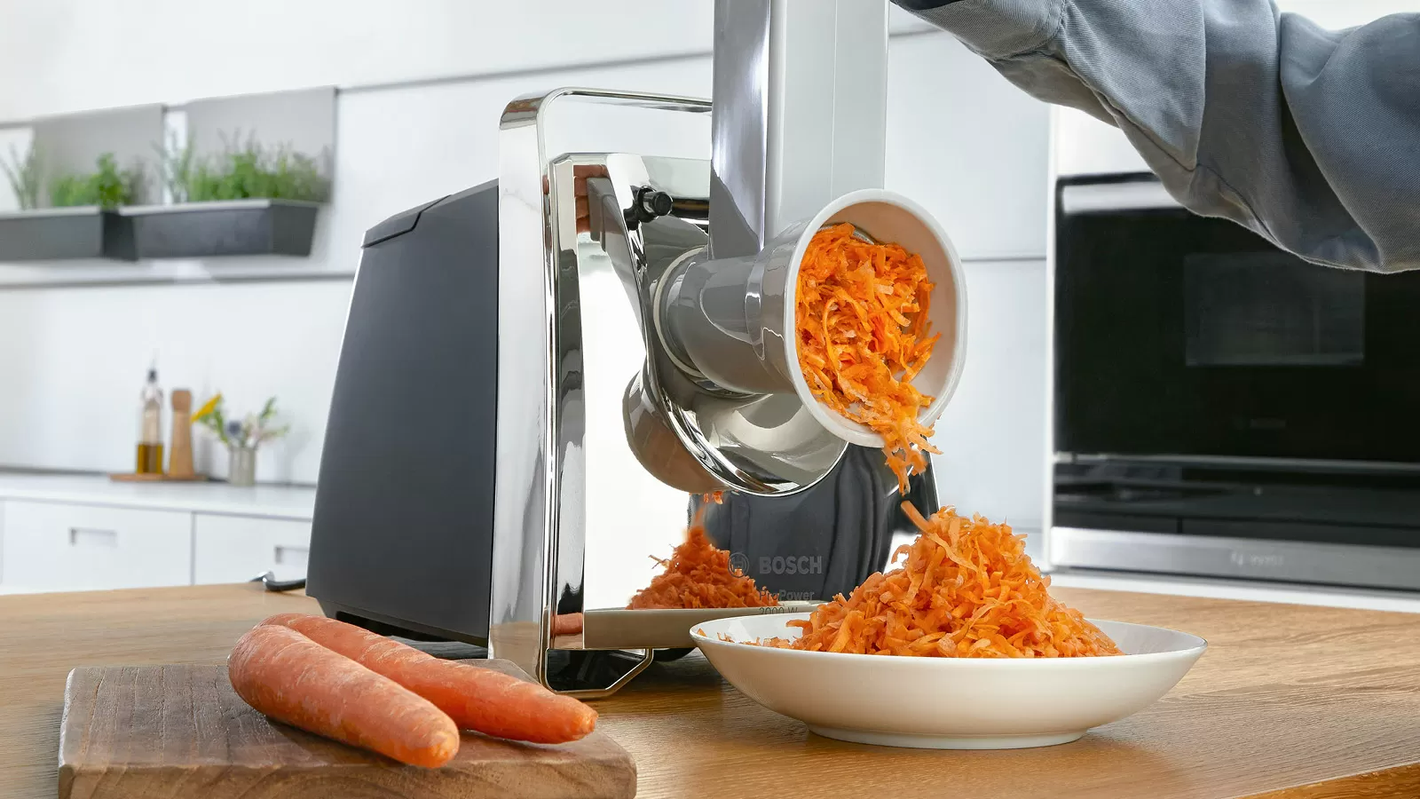 Egy ételreszelő, amivel sárgarépát reszelnek egy tányérba.