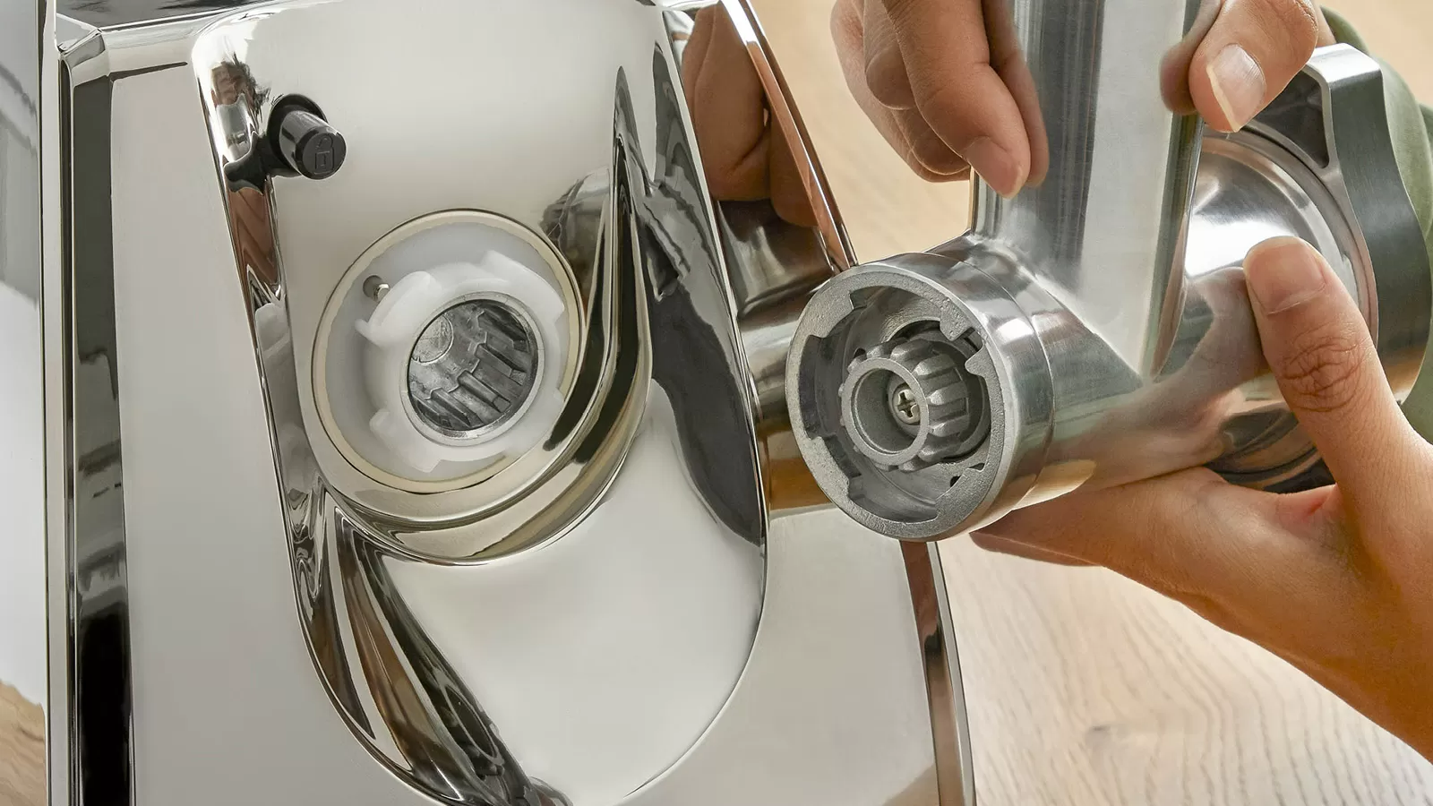 Egy személy közeli képe, amint egy húsdarálót szerel össze fényes fém alkatrészekkel.