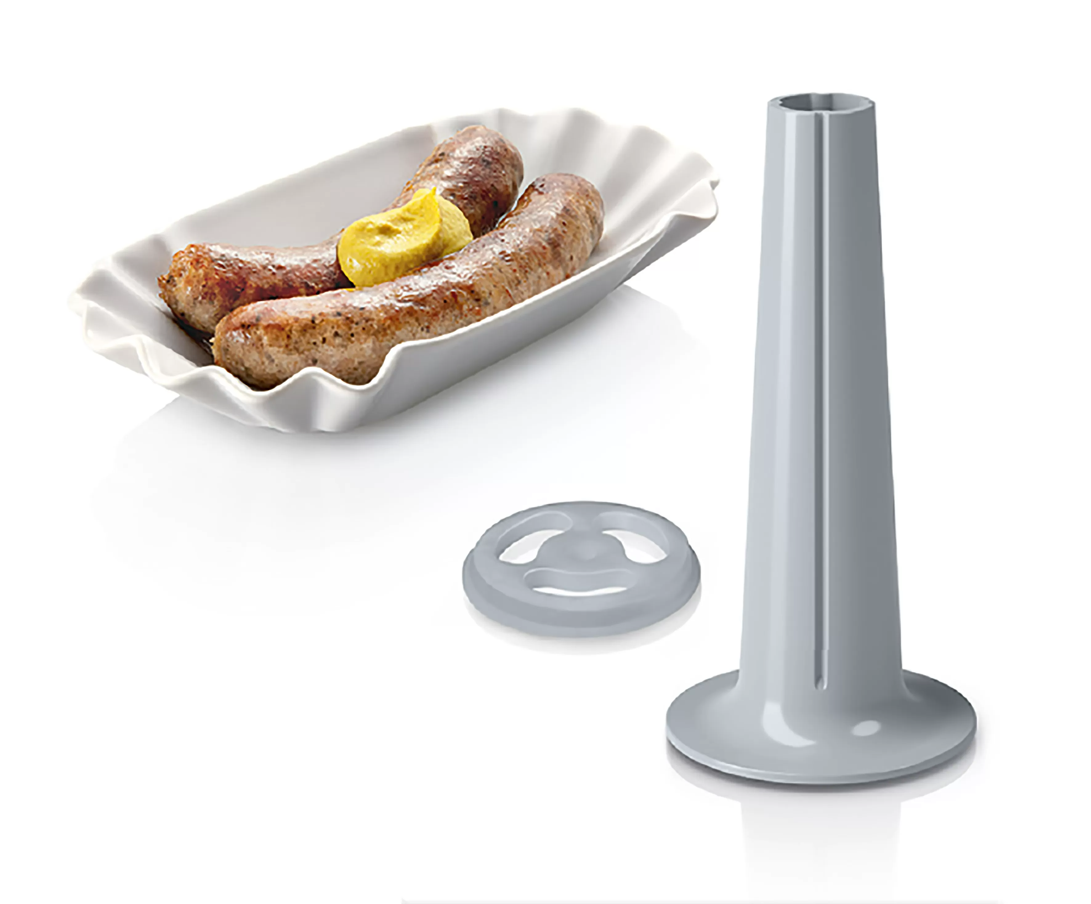 Kolbász mustárral egy tányéron, egy szürke kúppal és egy gyűrű alakú tárggyal.