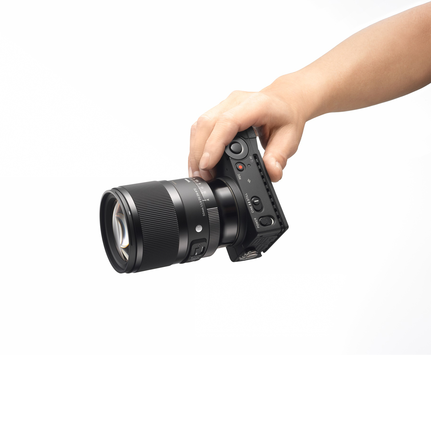Mano che tiene una fotocamera nera con un obiettivo grande. La fotocamera è angolata e l'obiettivo punta verso l'osservatore.