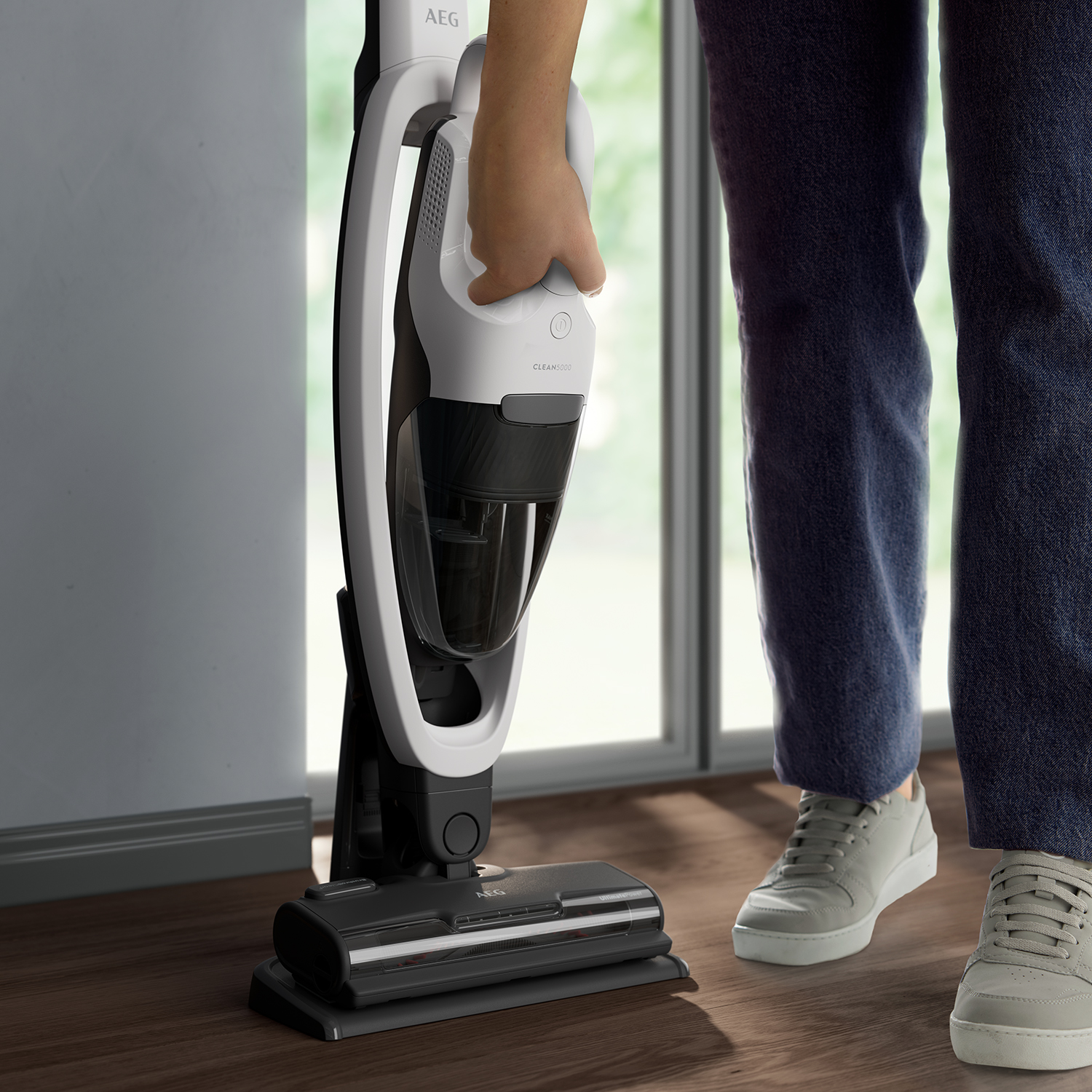 A person using a white and black AEG vacuum cleaner on a wooden floor.
