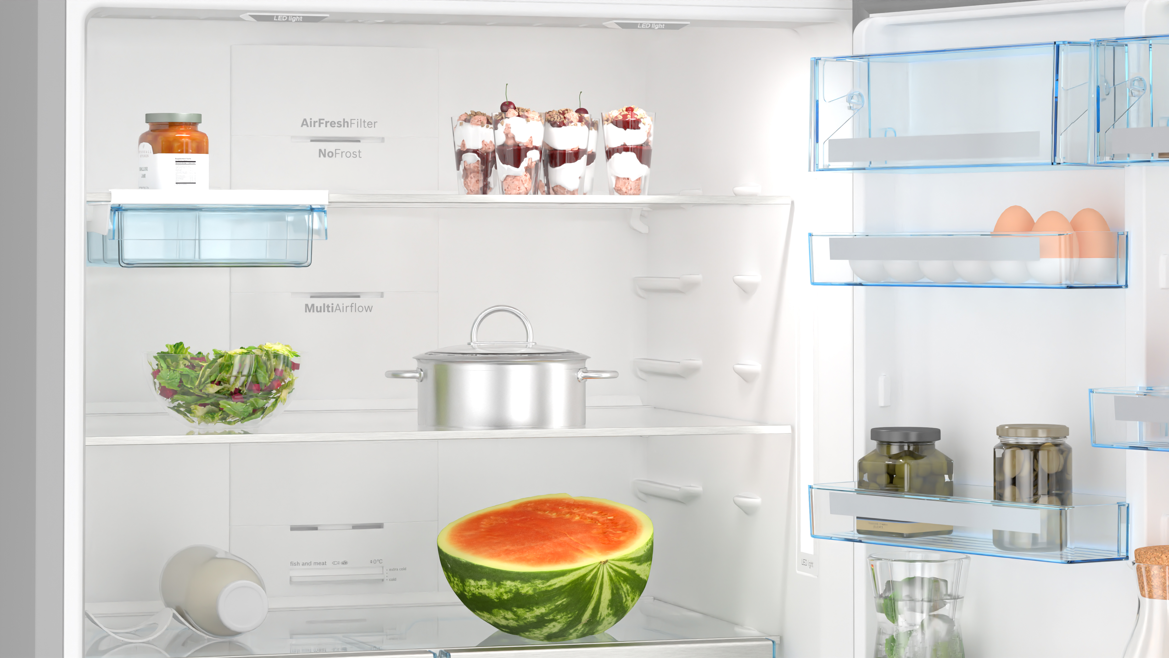 Offener Kühlschrank gefüllt mit Lebensmitteln: Salat, Wassermelone, Desserts und mehr.