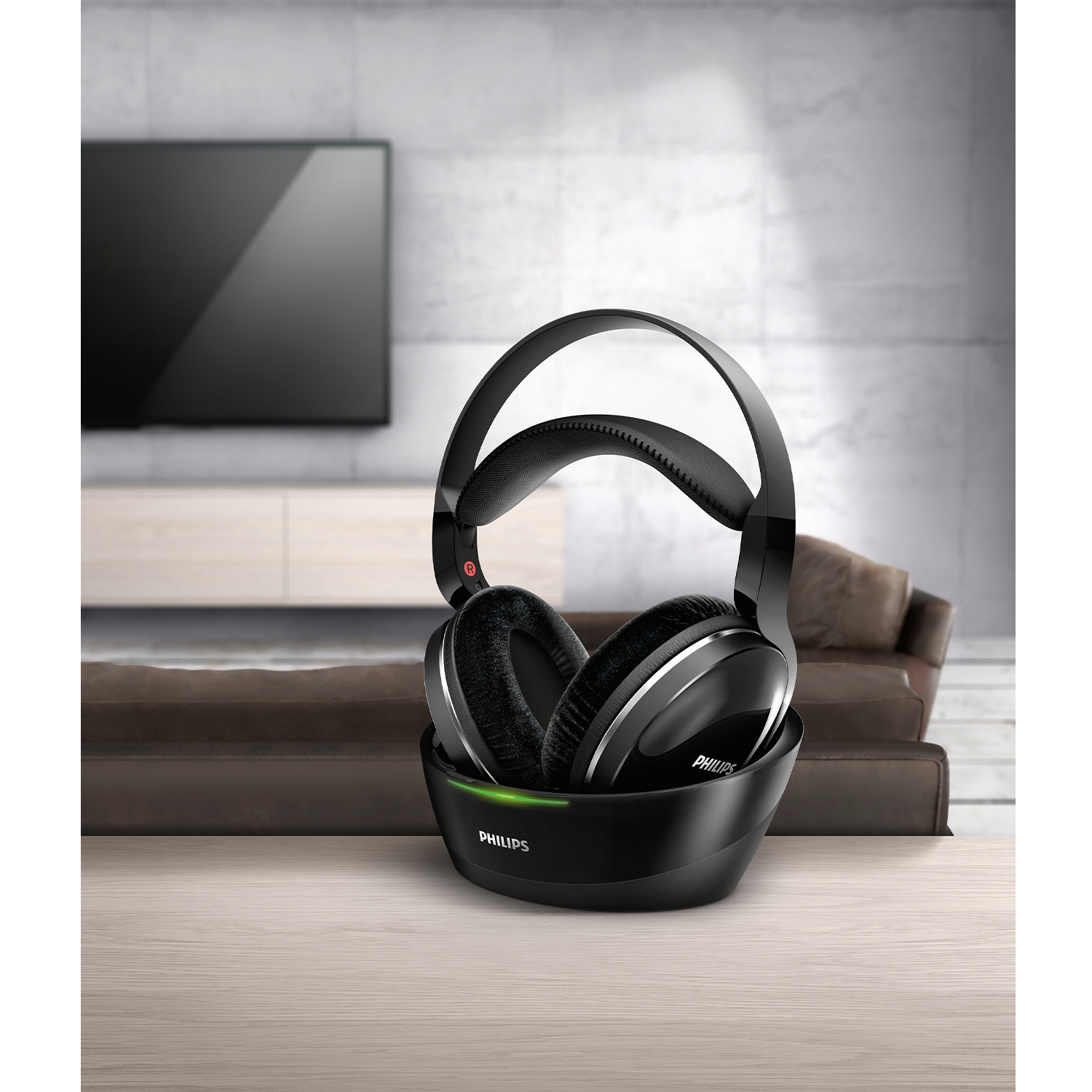 Cuffie Philips nere su una base, su un tavolo di legno. TV e divano visibili sullo sfondo.