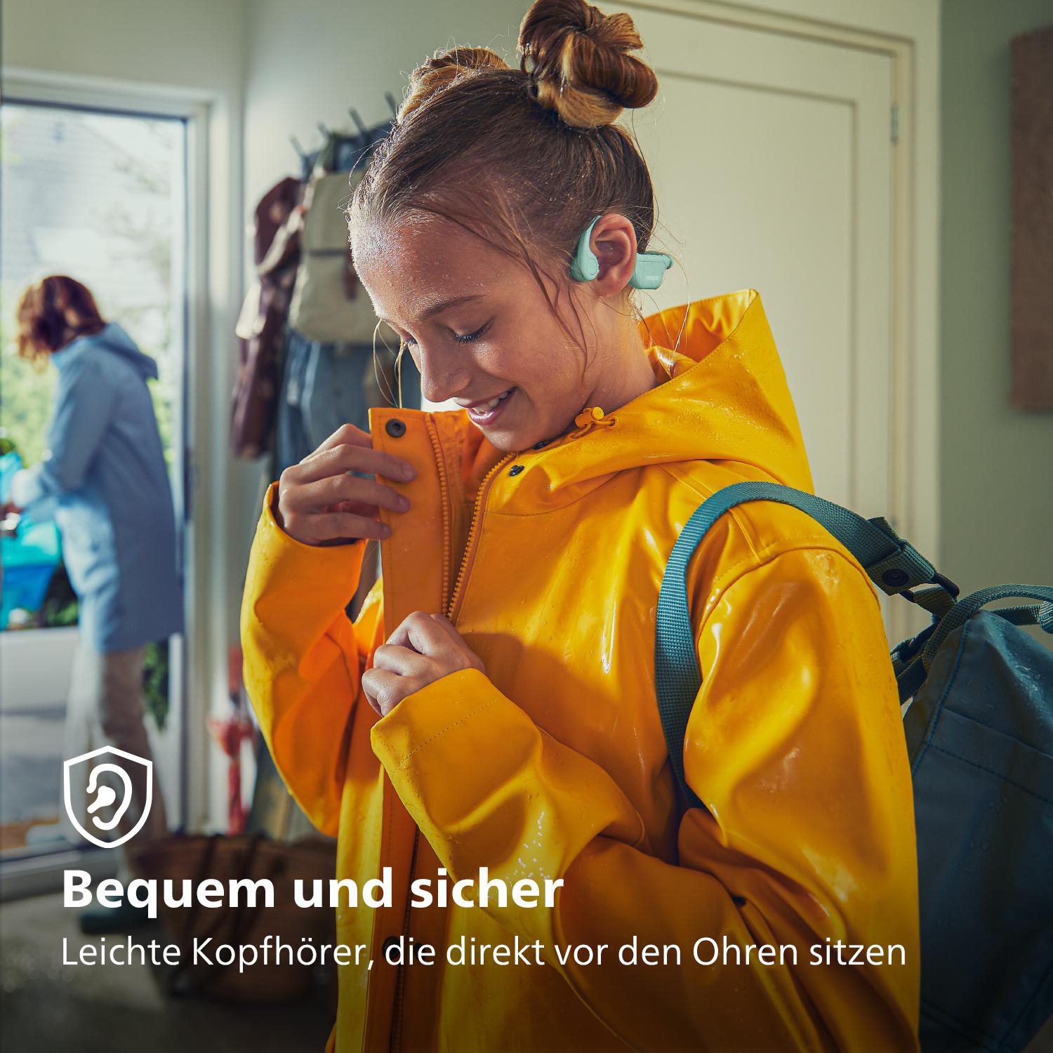 Ein Mädchen mit gelbem Regenmantel und Hörgeräten lächelt. Text: 