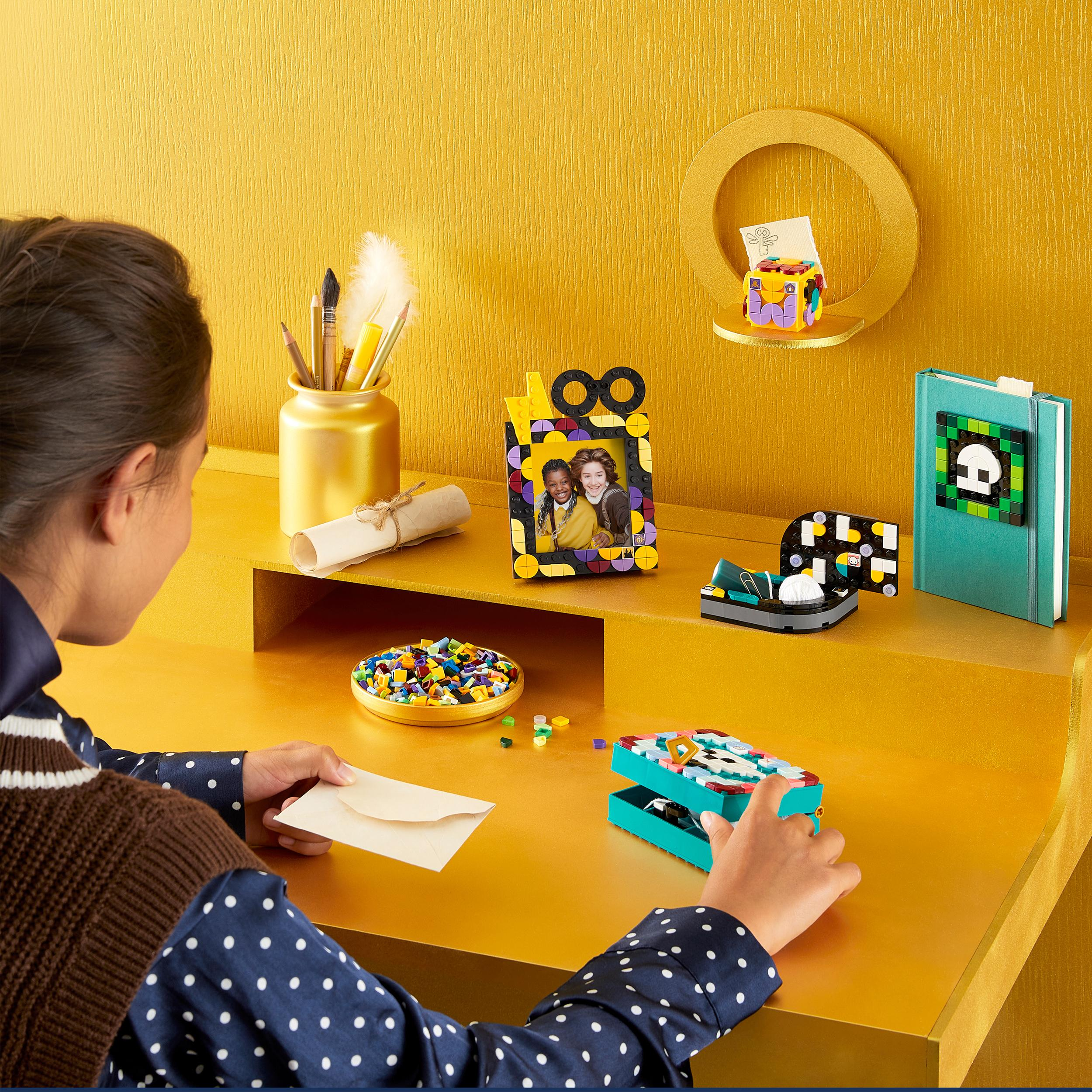 Mädchen an einem Schreibtisch mit Lego-Kreationen und Kunstbedarf.
