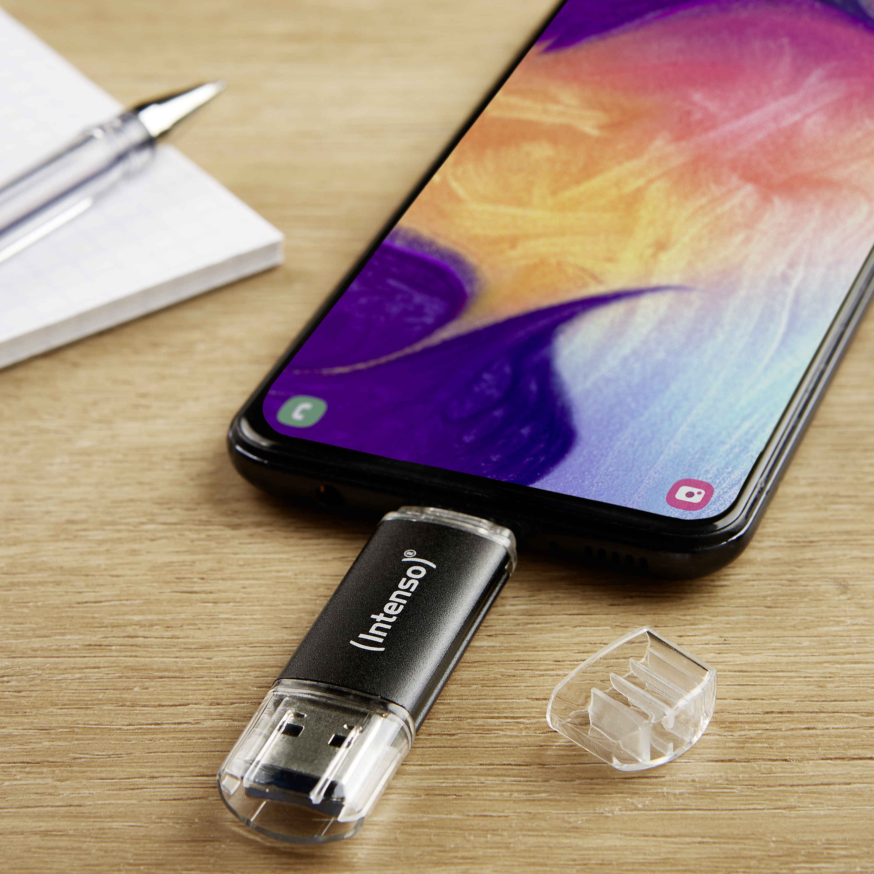 Fekete USB meghajtó egy színes telefonba dugva.