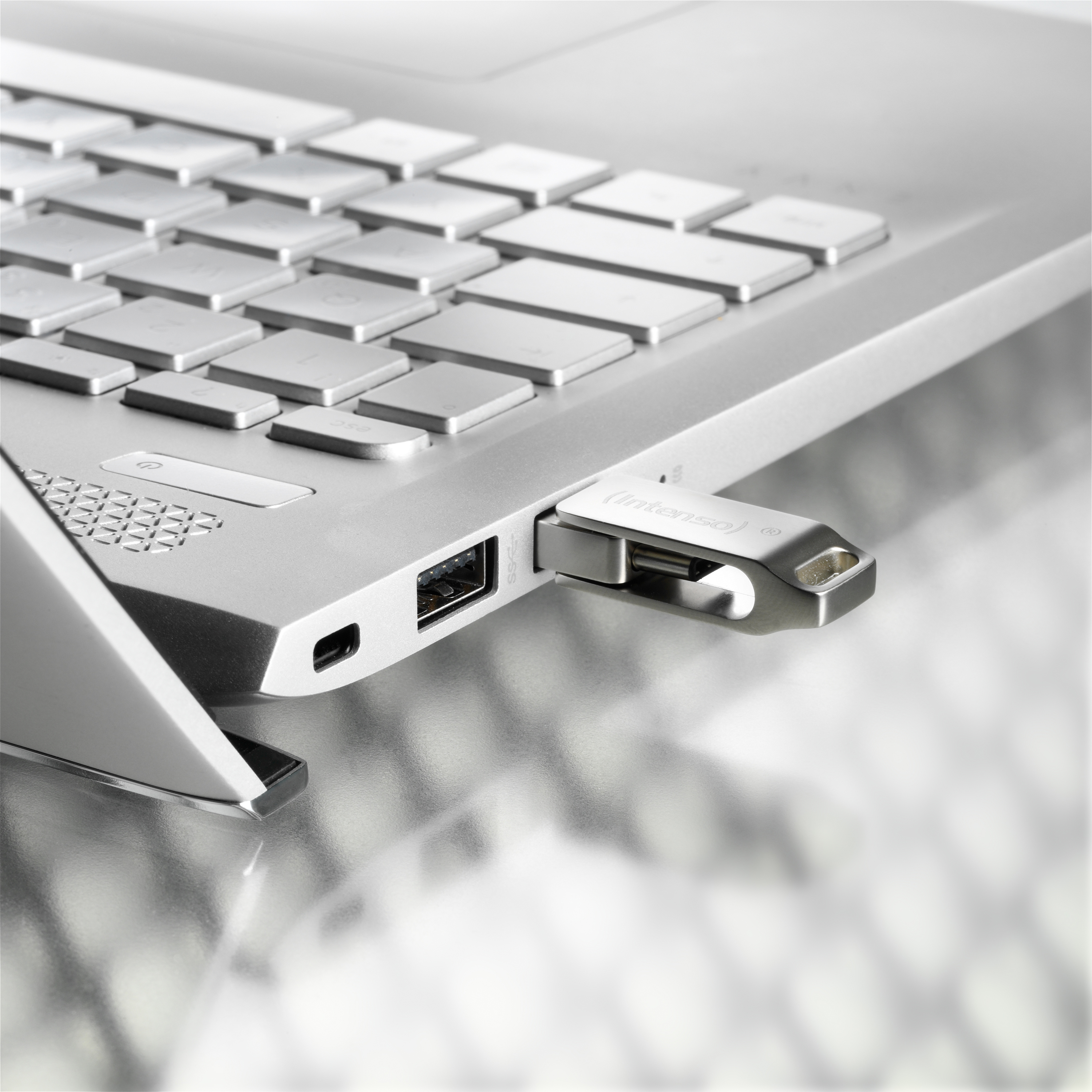 Ezüst laptop, USB-meghajtóval az oldalán. A billentyűzet látható.