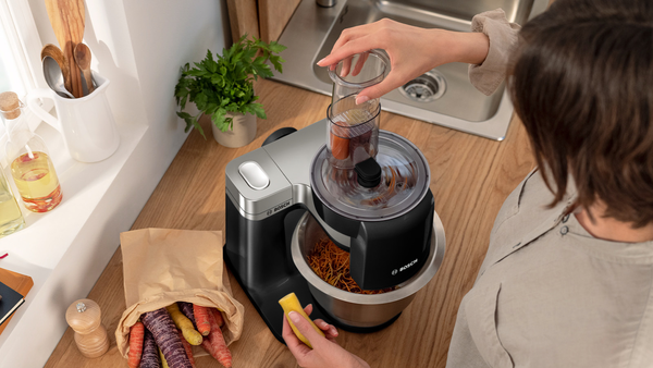 Bir kadın bir Bosch mutfak robotuna malzemeler ekliyor.