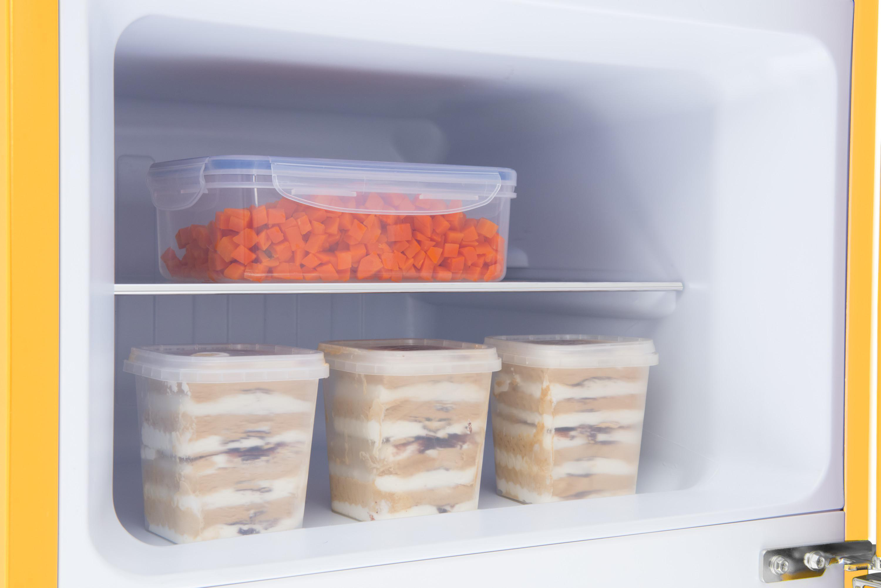 In einem gelben Kühlschrank: ein Behälter mit Karotten und Eiscremebehälter.