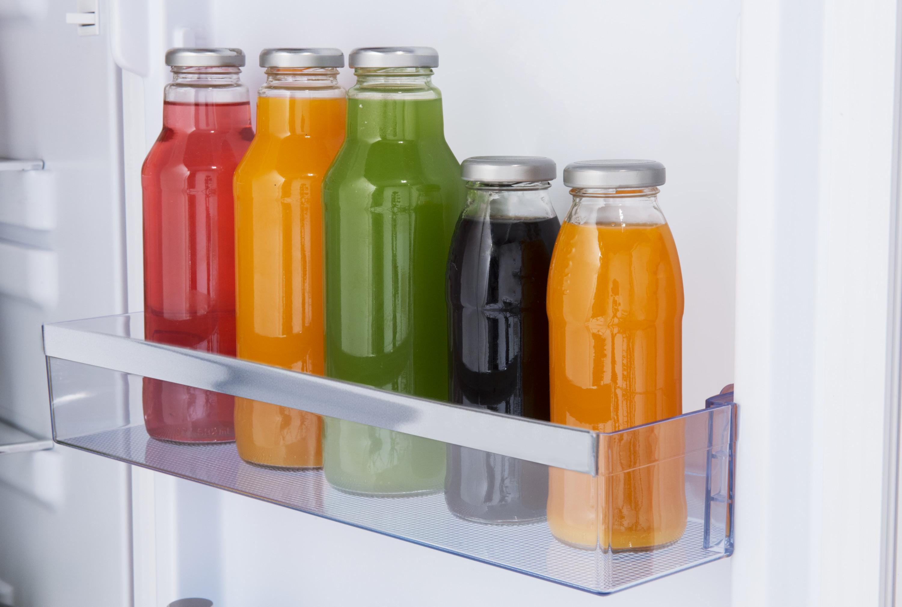 Ein Kühlschrankregal mit bunten Saftflaschen. Die Flaschen sind rot, orange, grün, schwarz und orange.