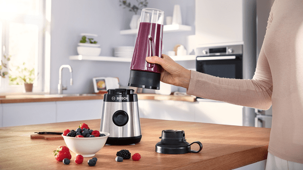 Masada bir kase meyve ile bir blender toplayan bir kişi.