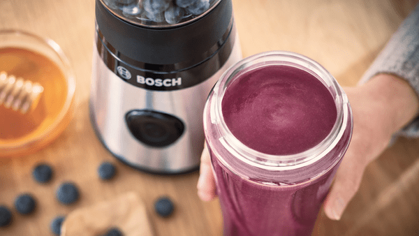 Ahşap bir masada smoothie ve yaban mersini ile blender. Bosch markası görünür durumda.
