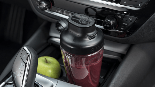 Yeşil elma ve araba konsolu ile siyah bir blender şişesi.