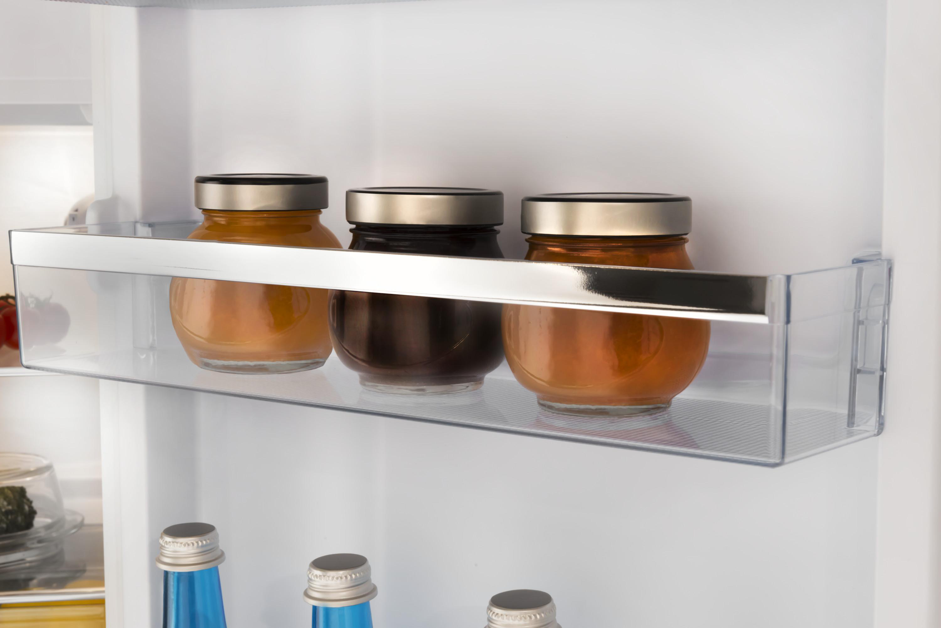 Drei Gläser mit Deckeln auf einem transparenten Regal in einem Kühlschrank. Weißes Innere.