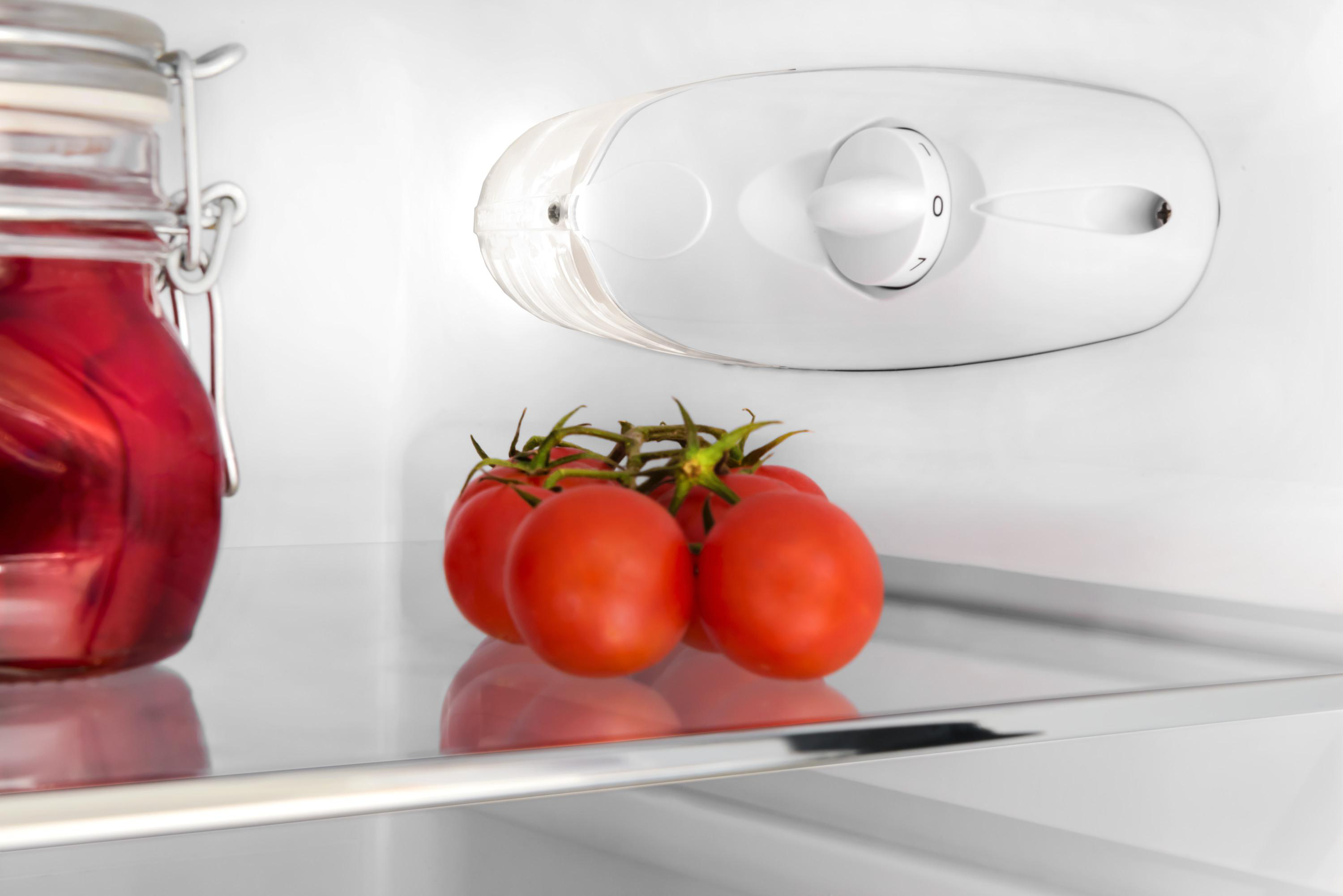 Nahaufnahme von Tomaten auf einem Regal in einem Kühlschrank. Ein weißes Zifferblatt ist ebenfalls sichtbar.