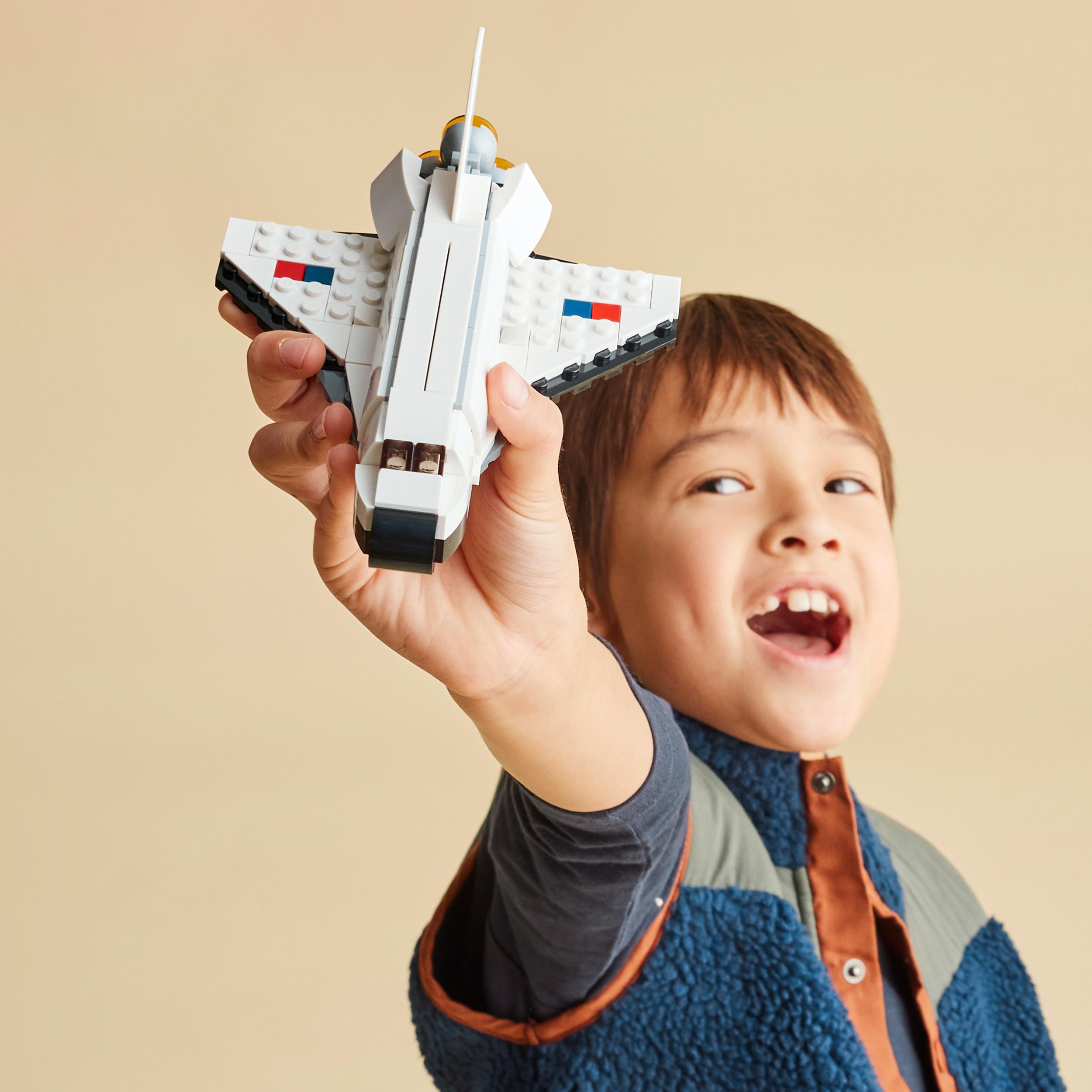 Ein Junge hält ein weiß-blaues Lego-Weltraumschiff. Er lächelt und schaut nach oben.