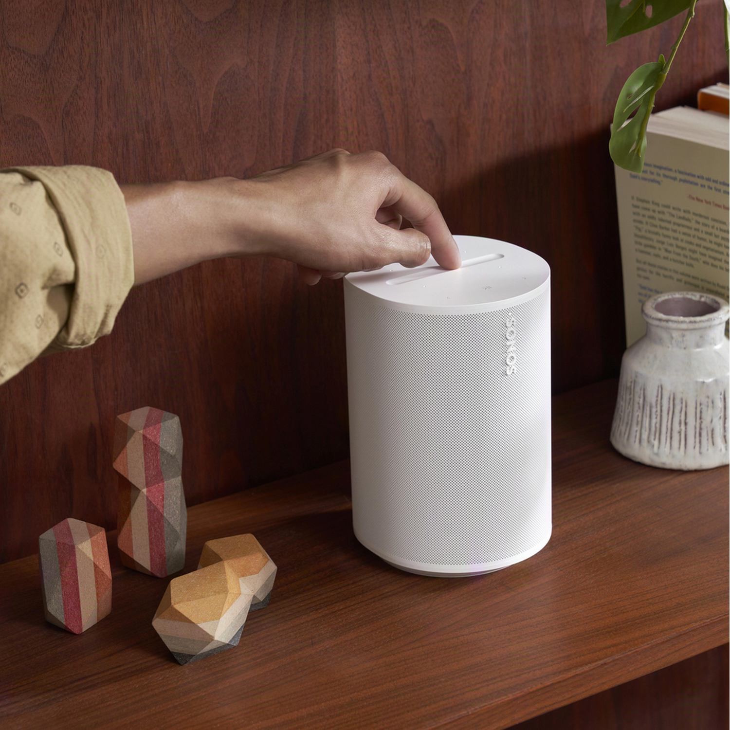 A white Sonos speaker on a wood surface next to geometric decor and a plant.