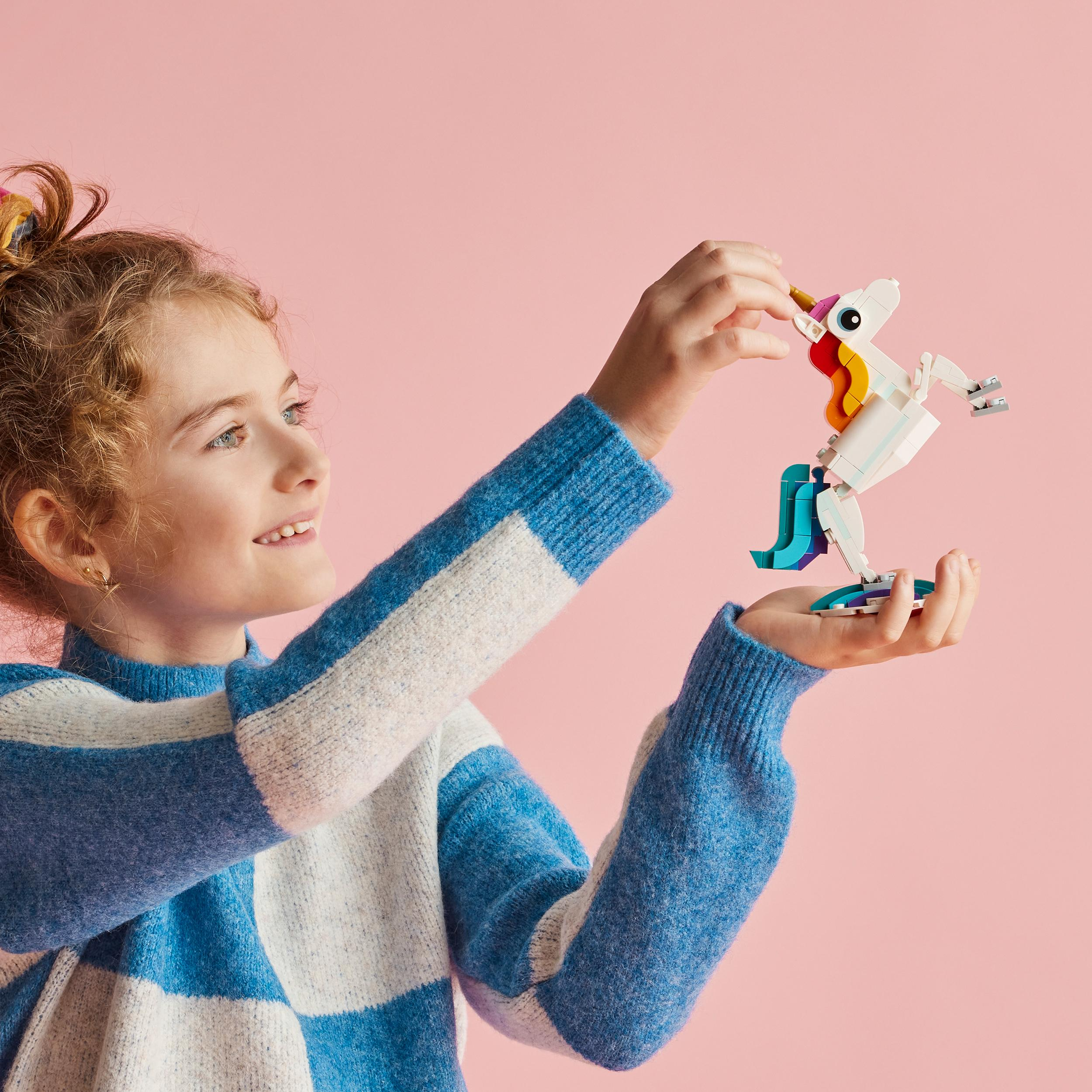 Ein Mädchen hält ein Lego-Einhorn. Es hat einen weißen Körper, bunte Mähne und blaue Basis.