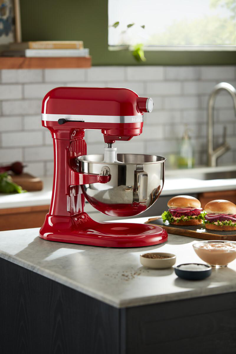 Roter KitchenAid Mixer auf Theke. Burger und Schüsseln mit Belägen daneben. Küchenszene.