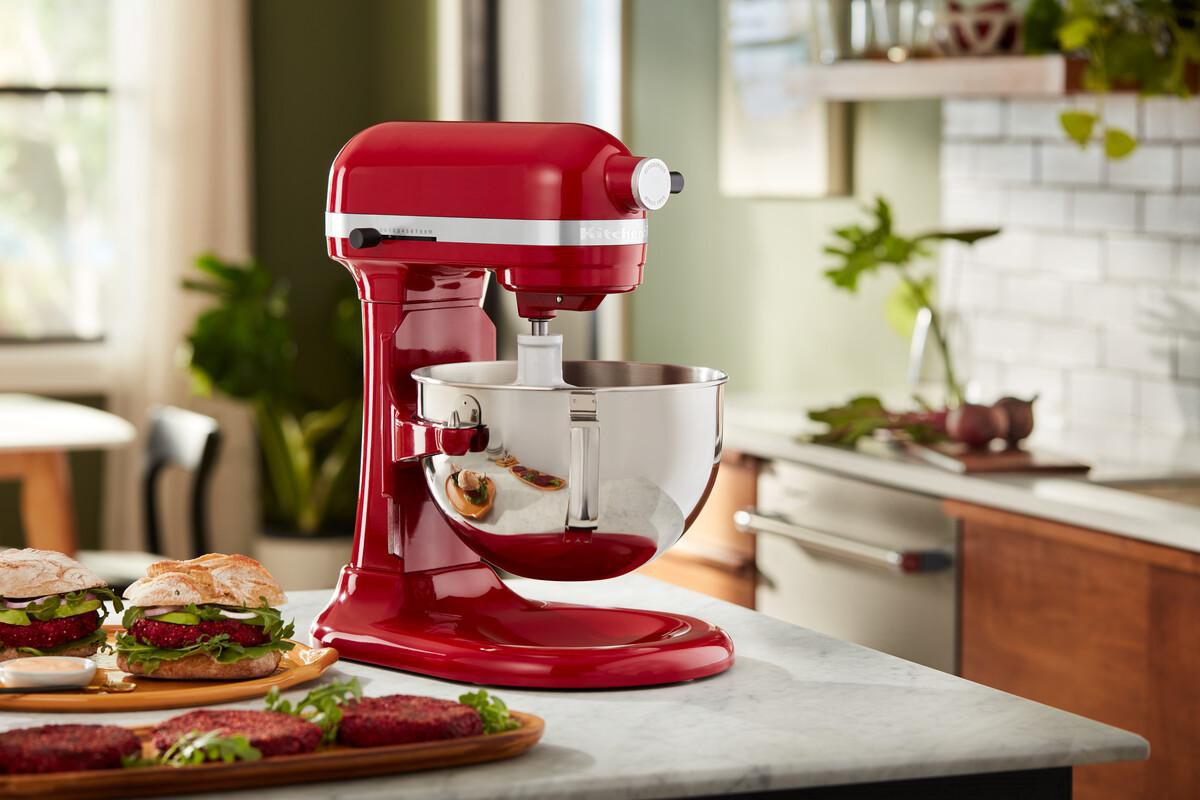 Roter KitchenAid Mixer mit Schüssel, Burger auf einem Tisch, in einer Küche.