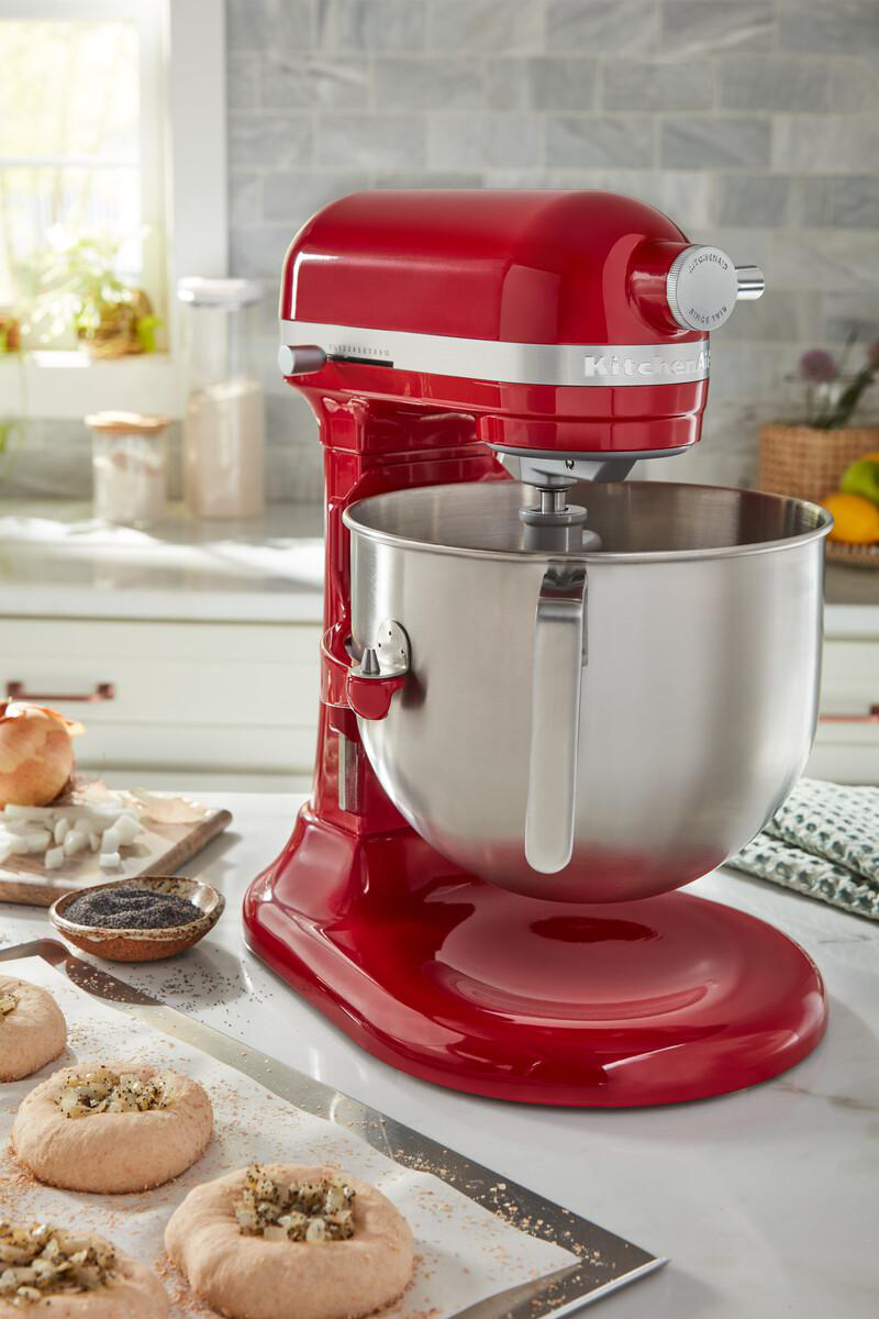 Roter KitchenAid-Mixer mit Metallschüssel, auf Marmorplatte. Zutaten und Essen sind drumherum.