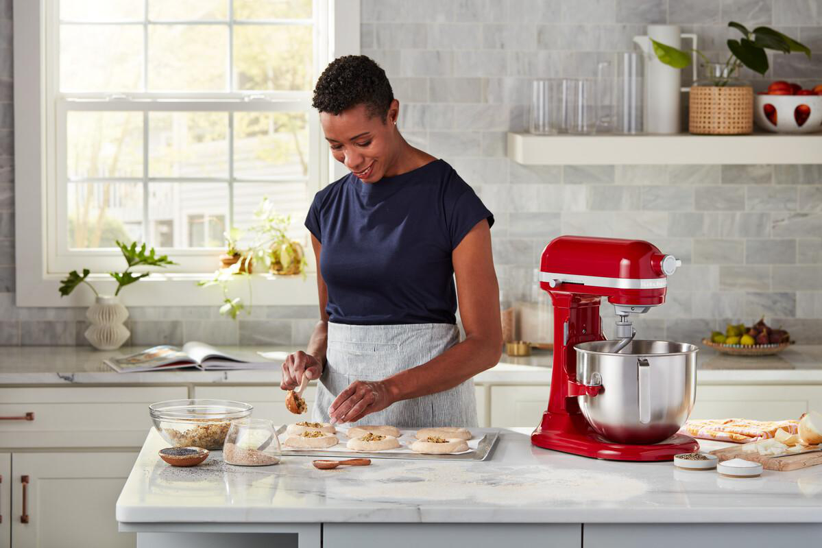 Frau in einer Küche, bereitet Essen in der Nähe eines roten KitchenAid Mixers zu.