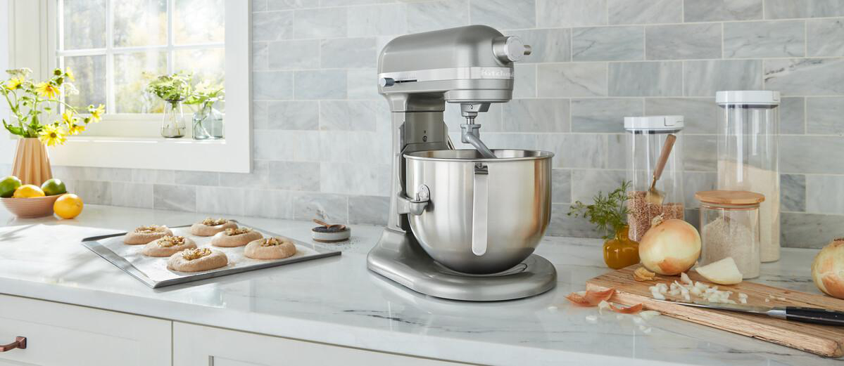 Eine Küchenszene mit einem Standmixer, Zutaten und einem Schneidebrett mit Zwiebeln und einem Messer.